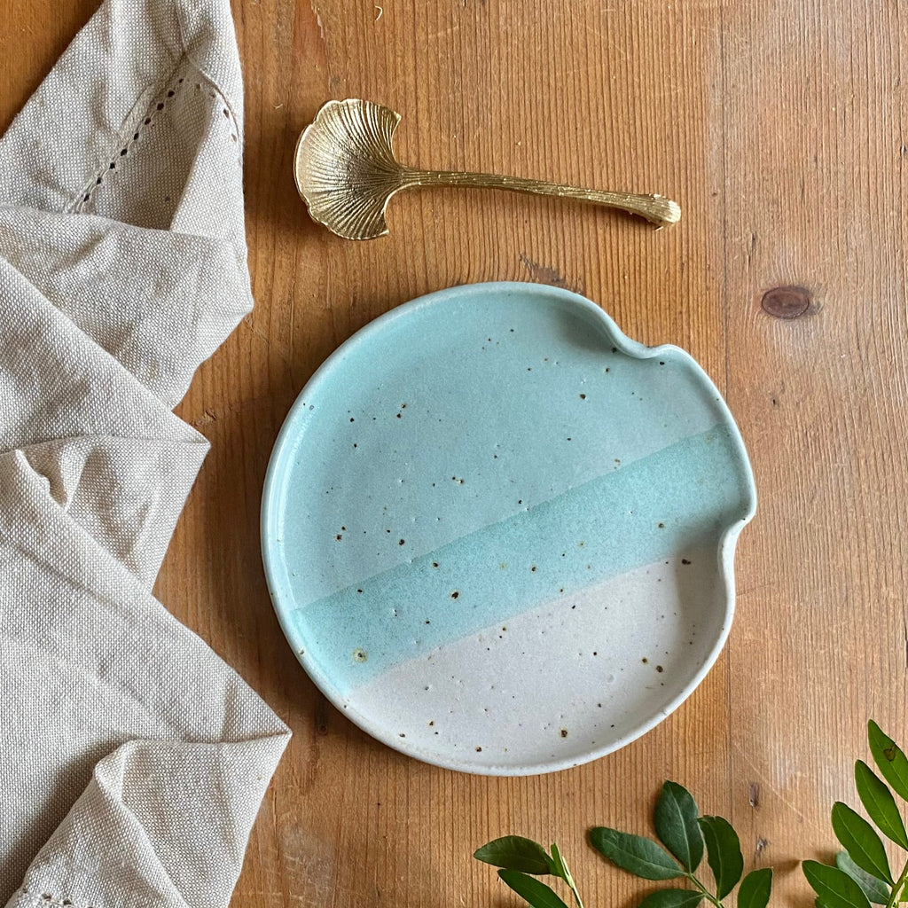 Handmade speckled ceramic dish with a light teal and off-white glaze, featuring a unique curved shape.