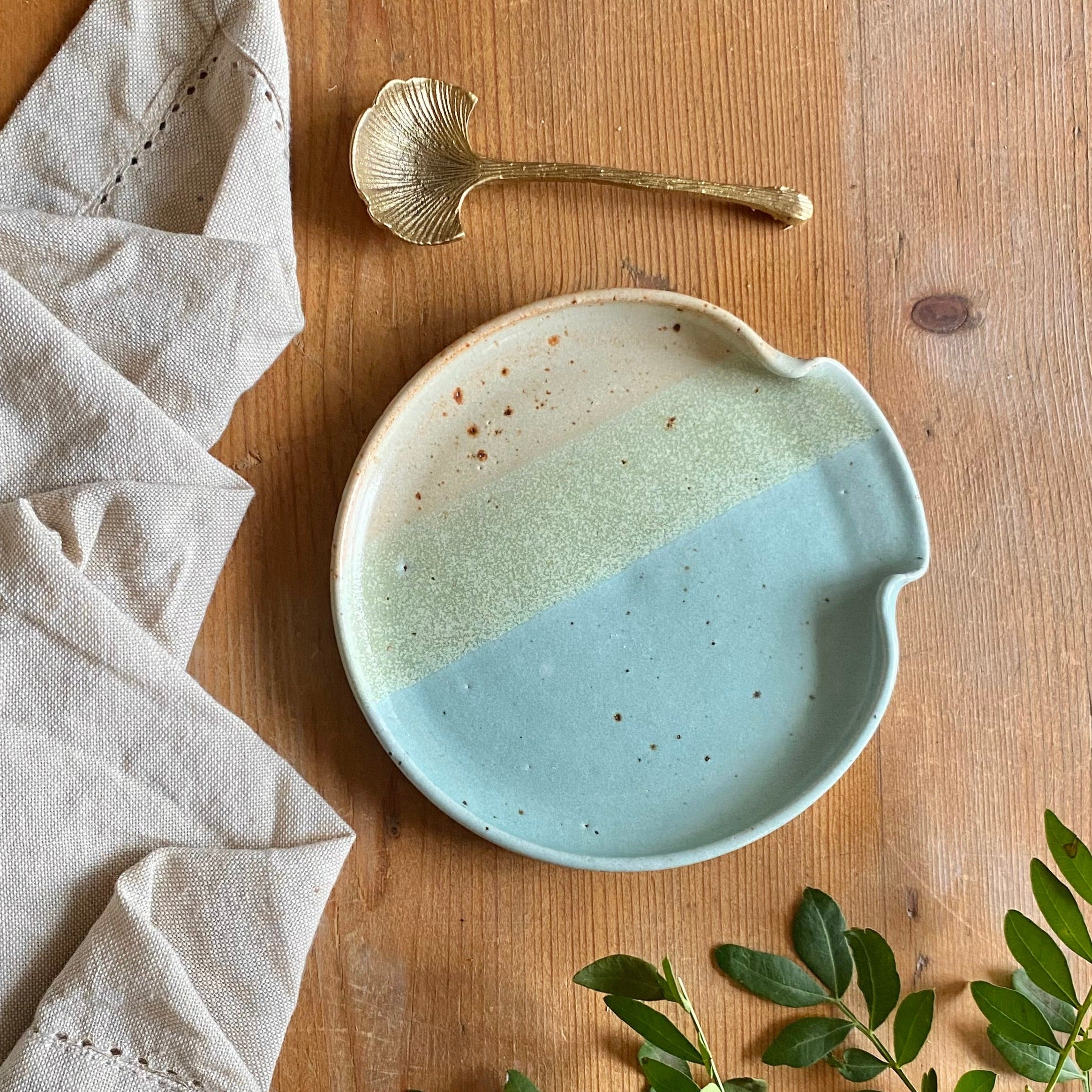 Round ceramic spoon rest with a speckled, three-toned glaze in beige, light green, and teal.