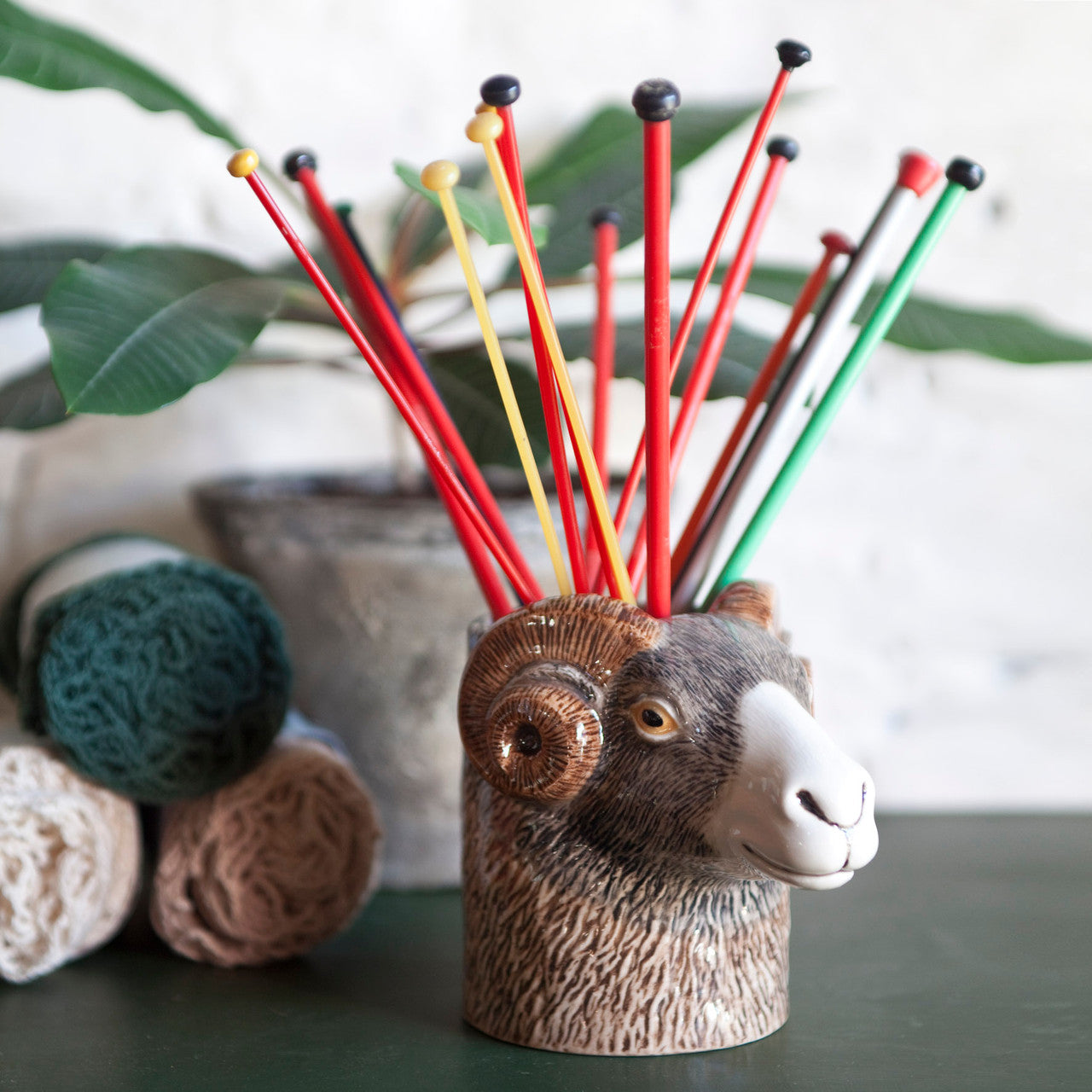 Ceramic ram's head holder containing assorted knitting needles.
