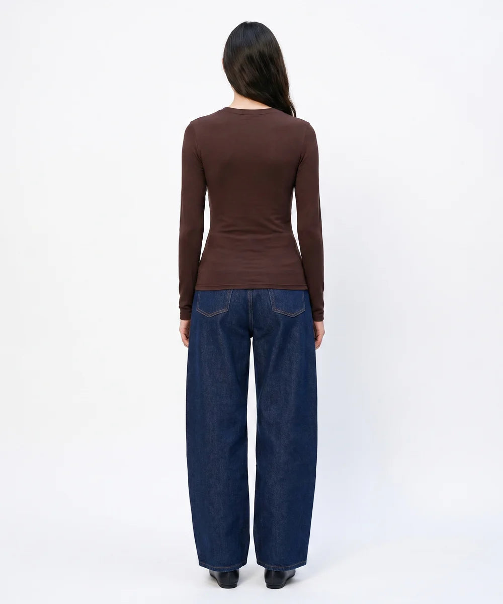A woman viewed from the back wearing a fitted brown long-sleeve top and dark blue wide-leg jeans against a plain white studio background.