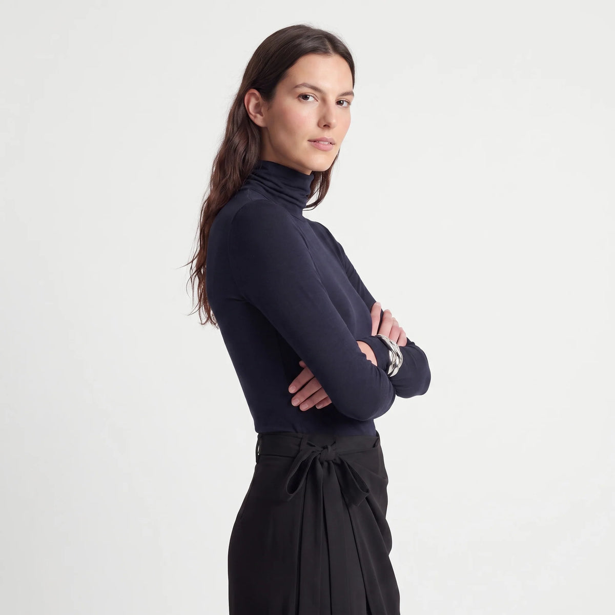 A woman modeling a dark navy blue mock neck long-sleeve top paired with black high-waisted wrap pants against a clean white studio background.
