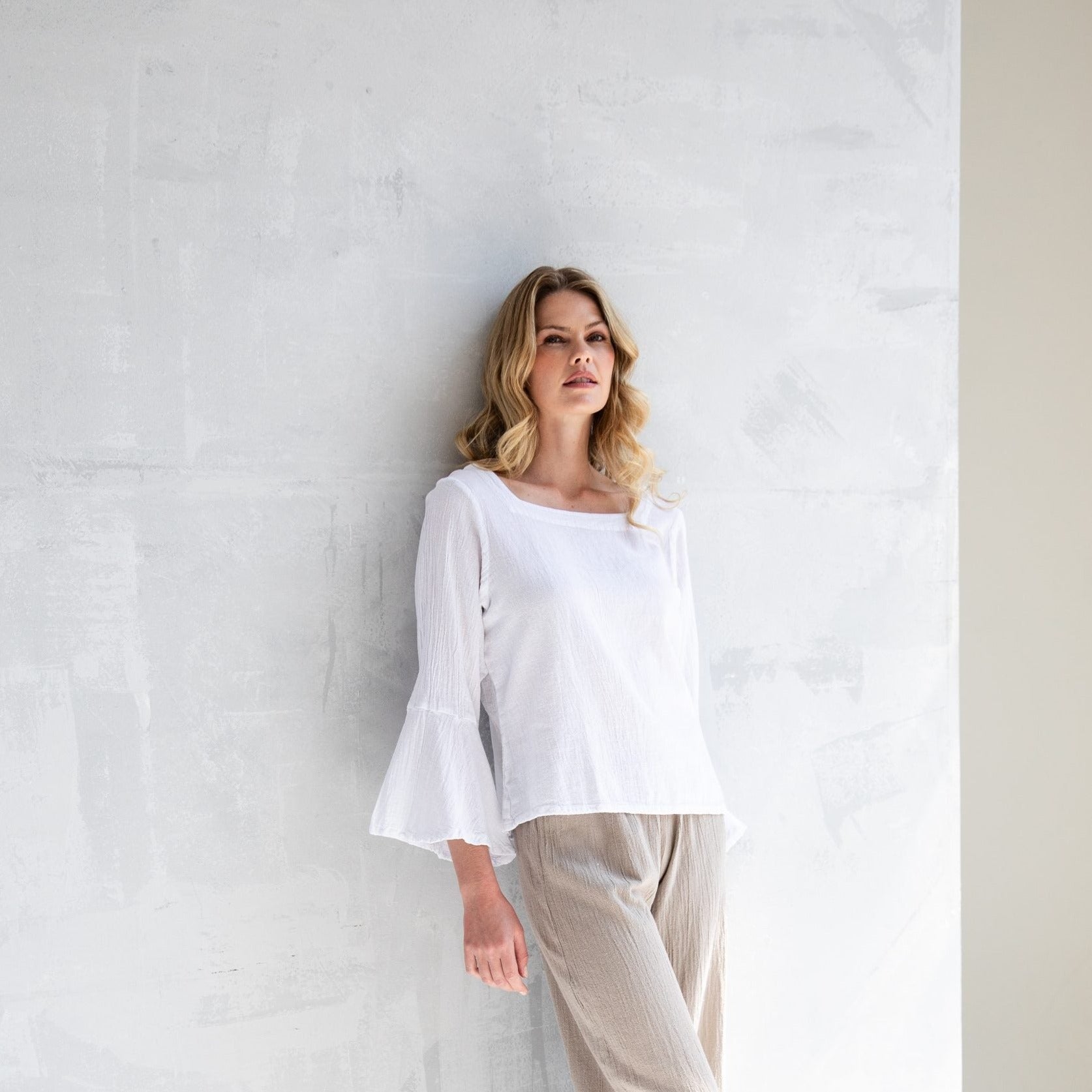 White bell-sleeve blouse with a square neckline, paired with light beige pants.