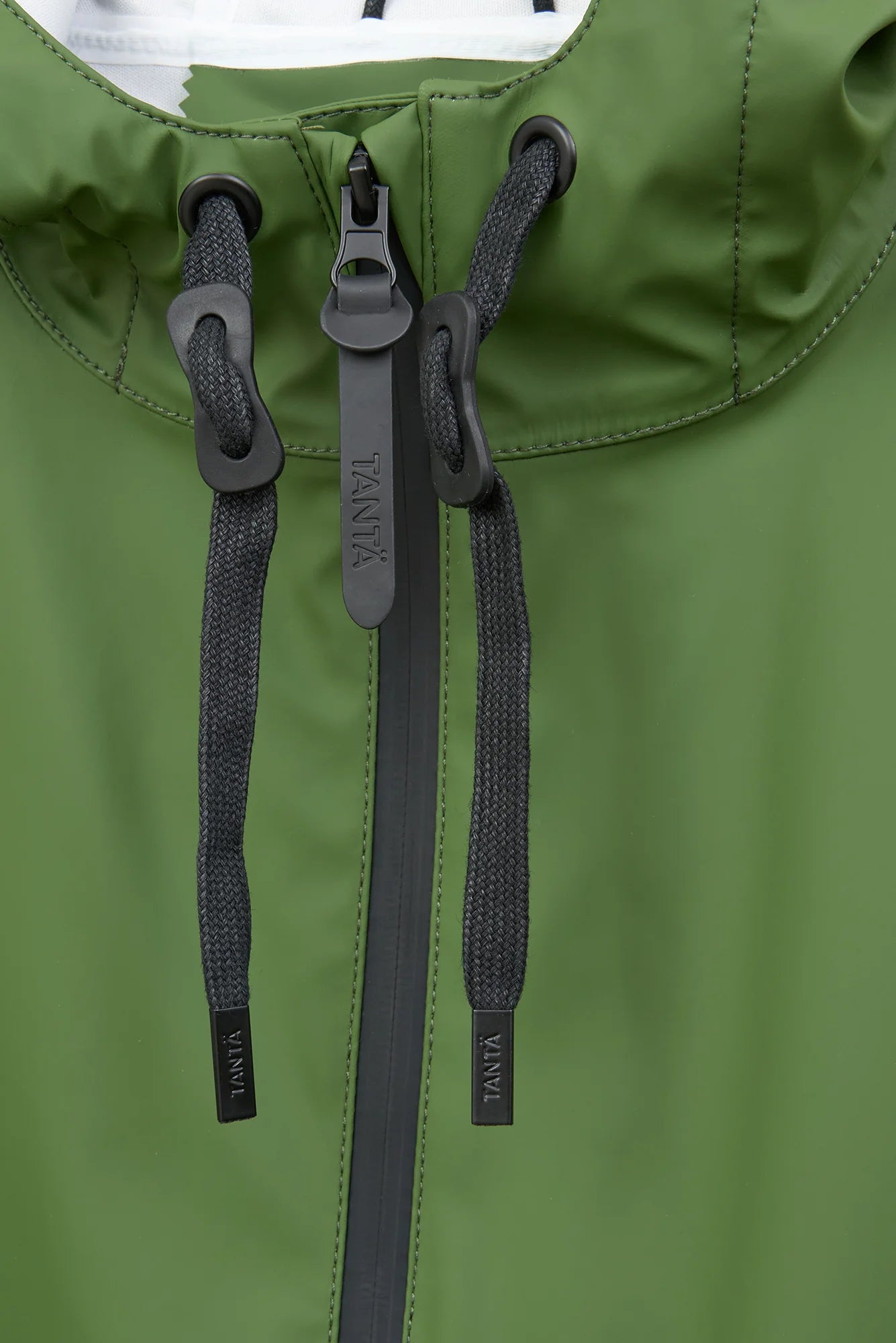 Close-up of an olive green hooded jacket with black drawstrings, a black zipper, and black plastic hardware. The zipper pull and drawstring tips show the brand name TAVIR.