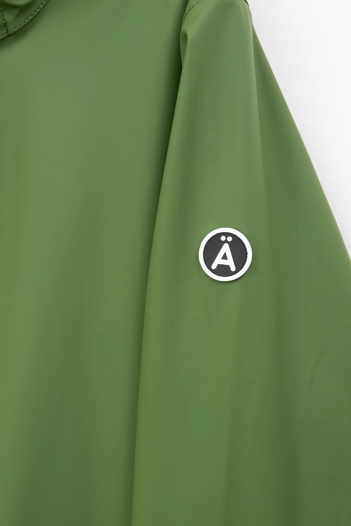 Close-up of an olive green jacket sleeve featuring a circular black and white logo patch with a stylized letter 'A' on the upper arm.