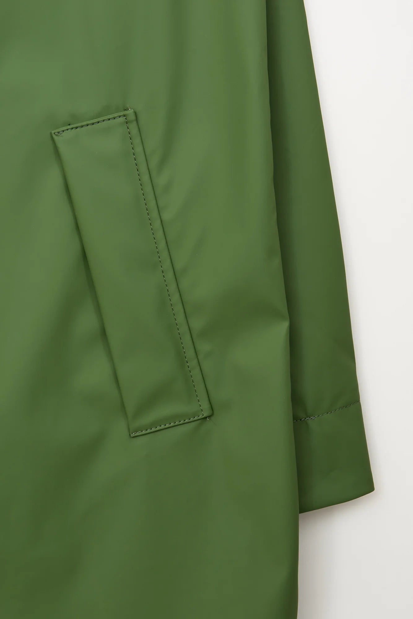 Close-up of an olive green garment showing a rectangular patch pocket with top stitching and a folded cuff on a plain light background.