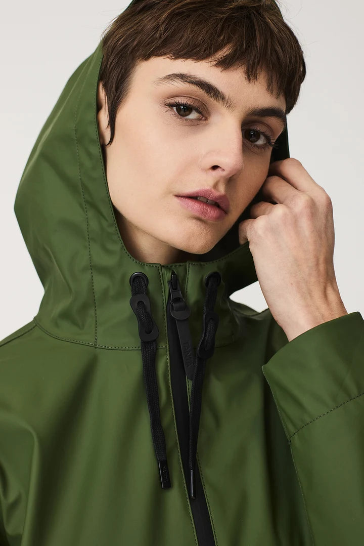 A close-up of a model wearing an olive green hooded rain jacket with black drawstrings and a black zipper, set against a plain light gray background.