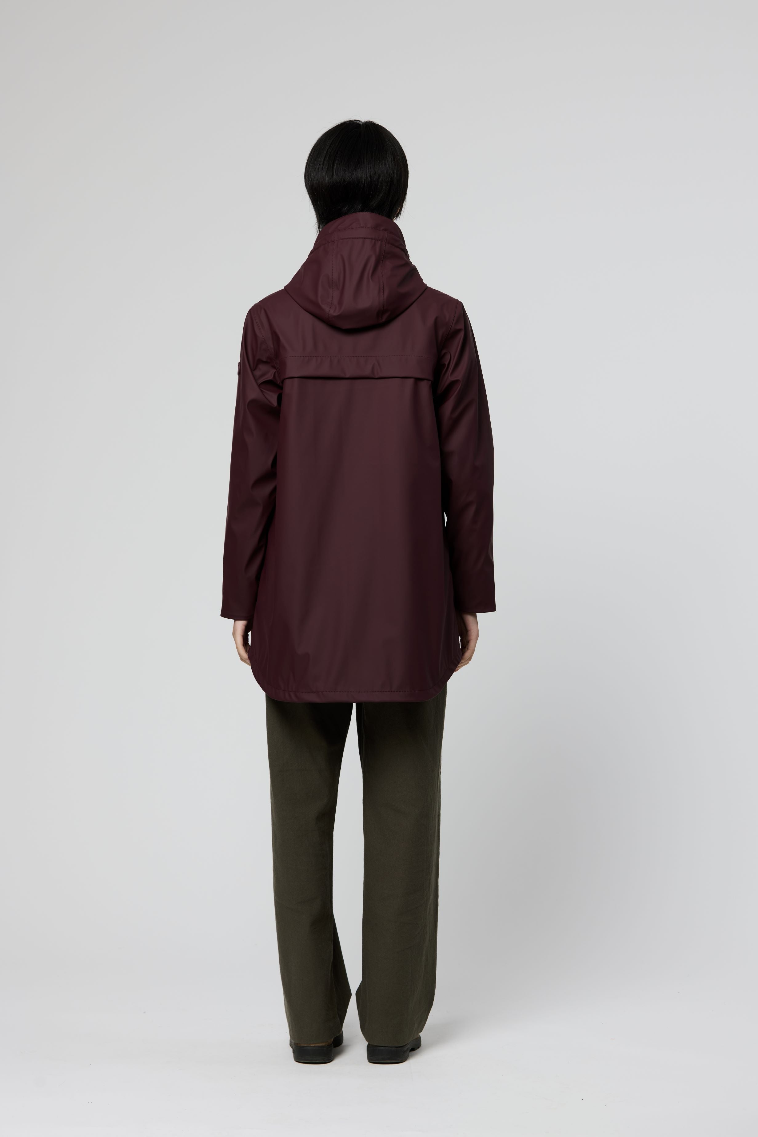 A person shown from the back wearing a hooded jacket in a deep burgundy shade, paired with olive green pants, against a light gray studio background.