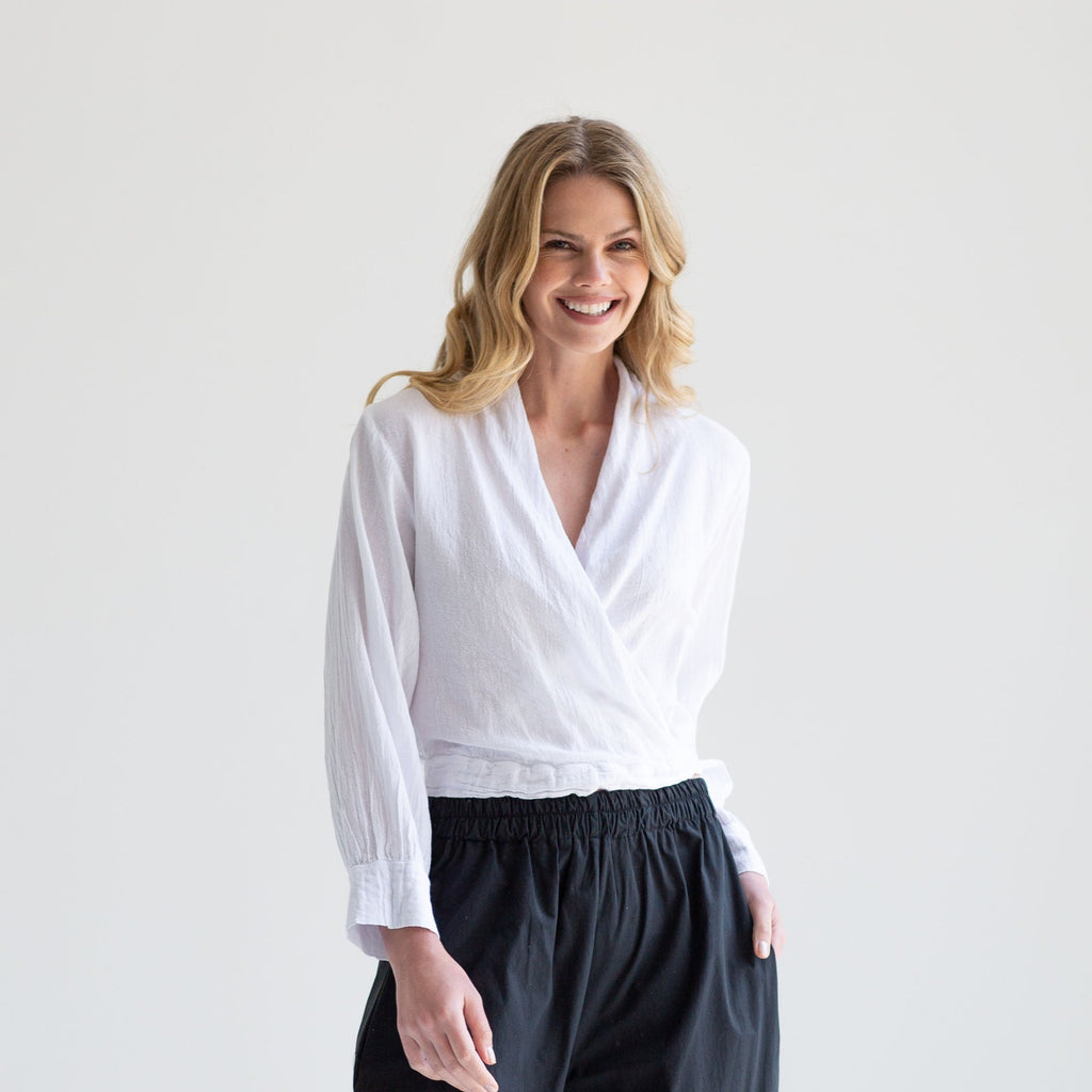 White wrap-style long-sleeve blouse with cuffed sleeves, worn with black drawstring pants.