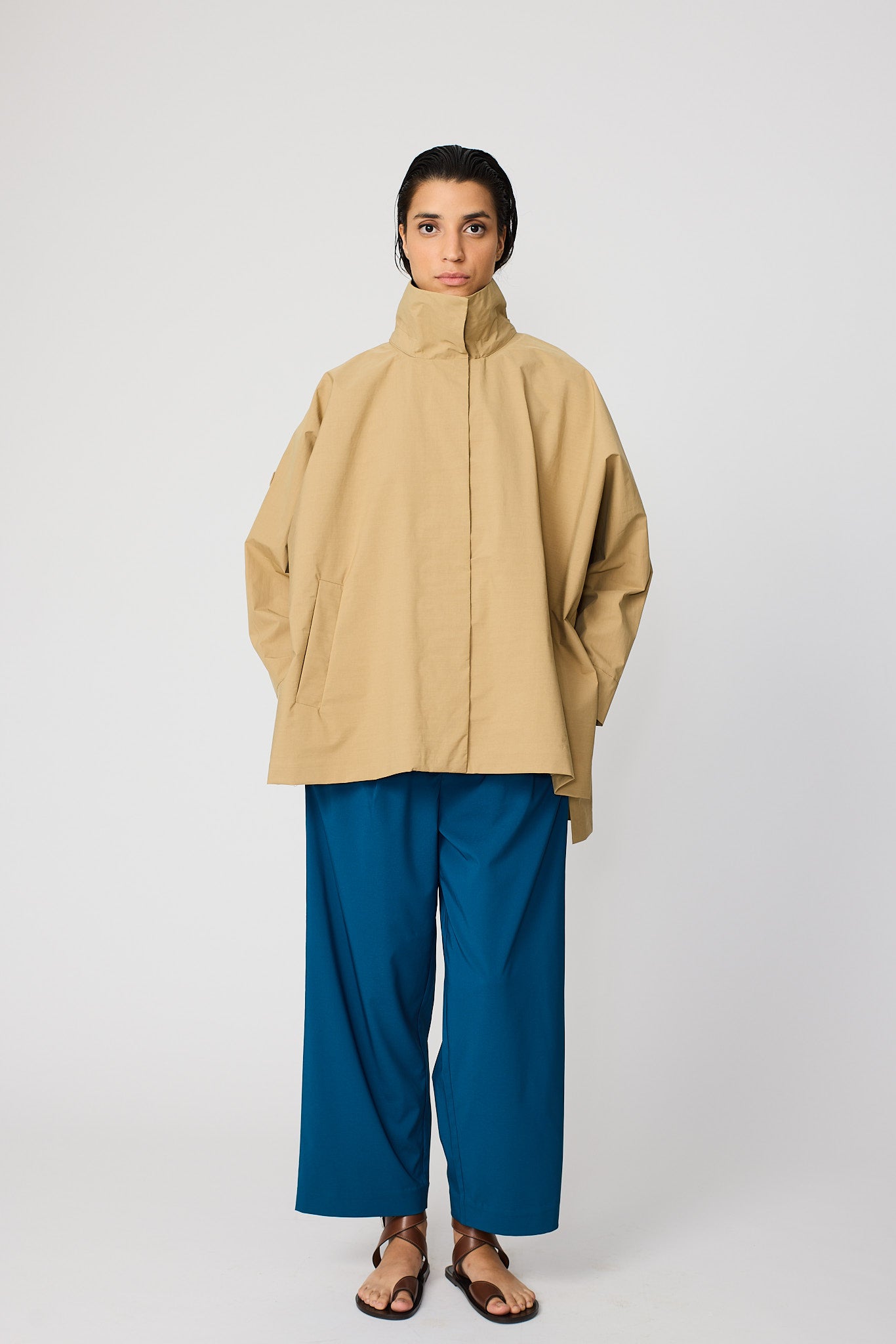 Person wearing a beige coat and blue pants on a white background