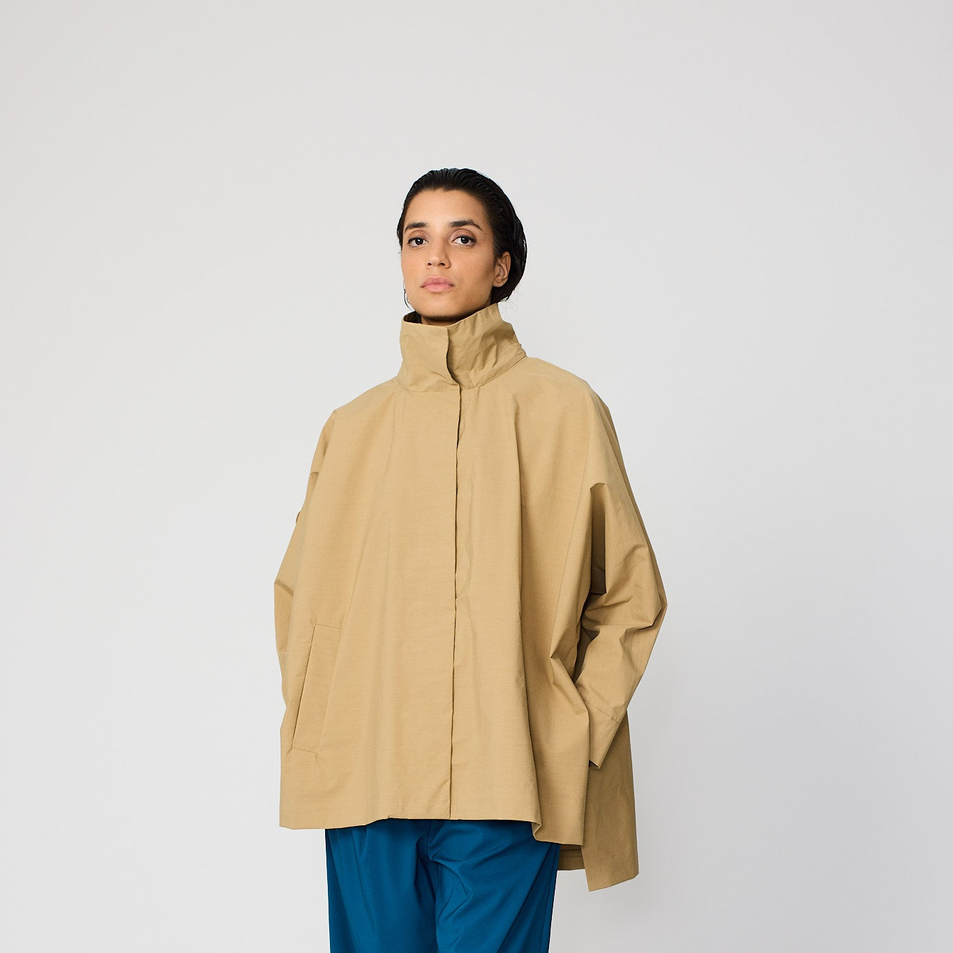 Person wearing a beige coat and blue pants on a white background