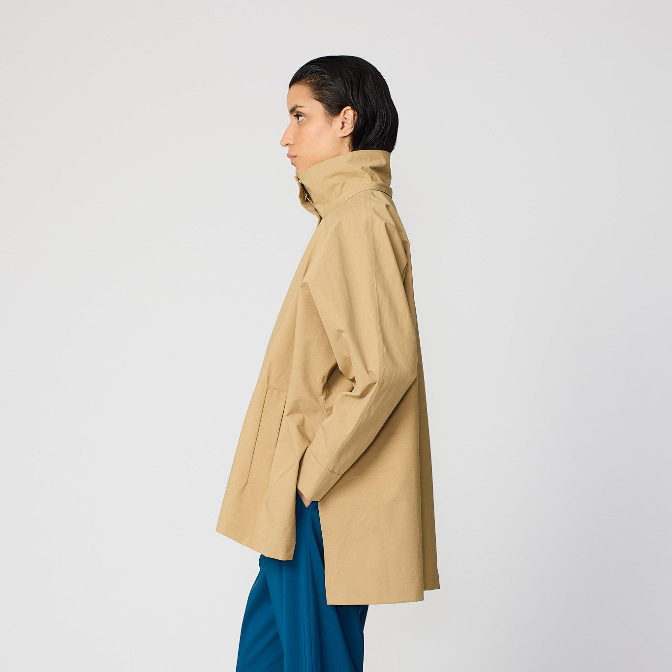 Woman wearing a beige coat and blue pants on a white background