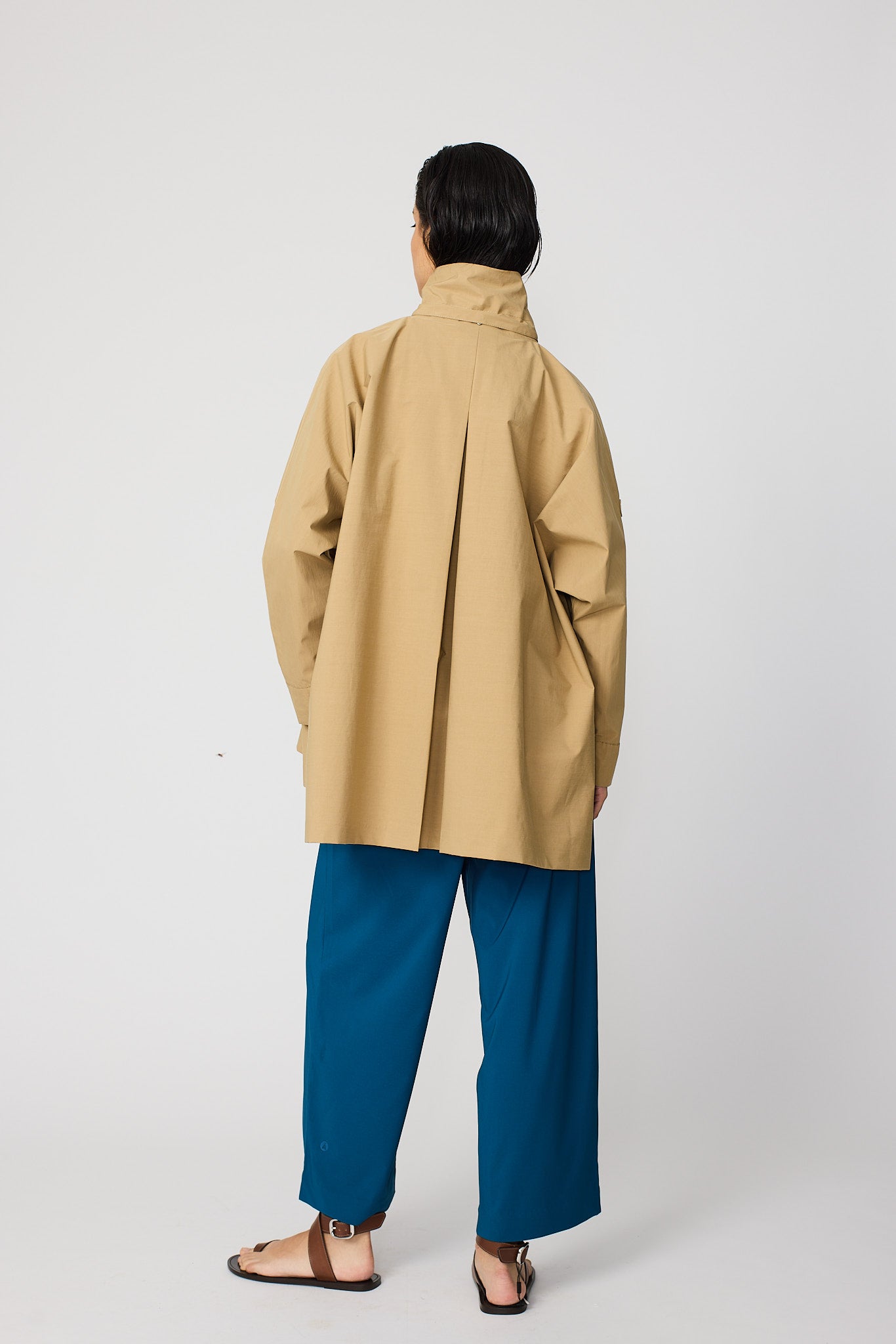 Person wearing a beige coat and blue pants on a white background