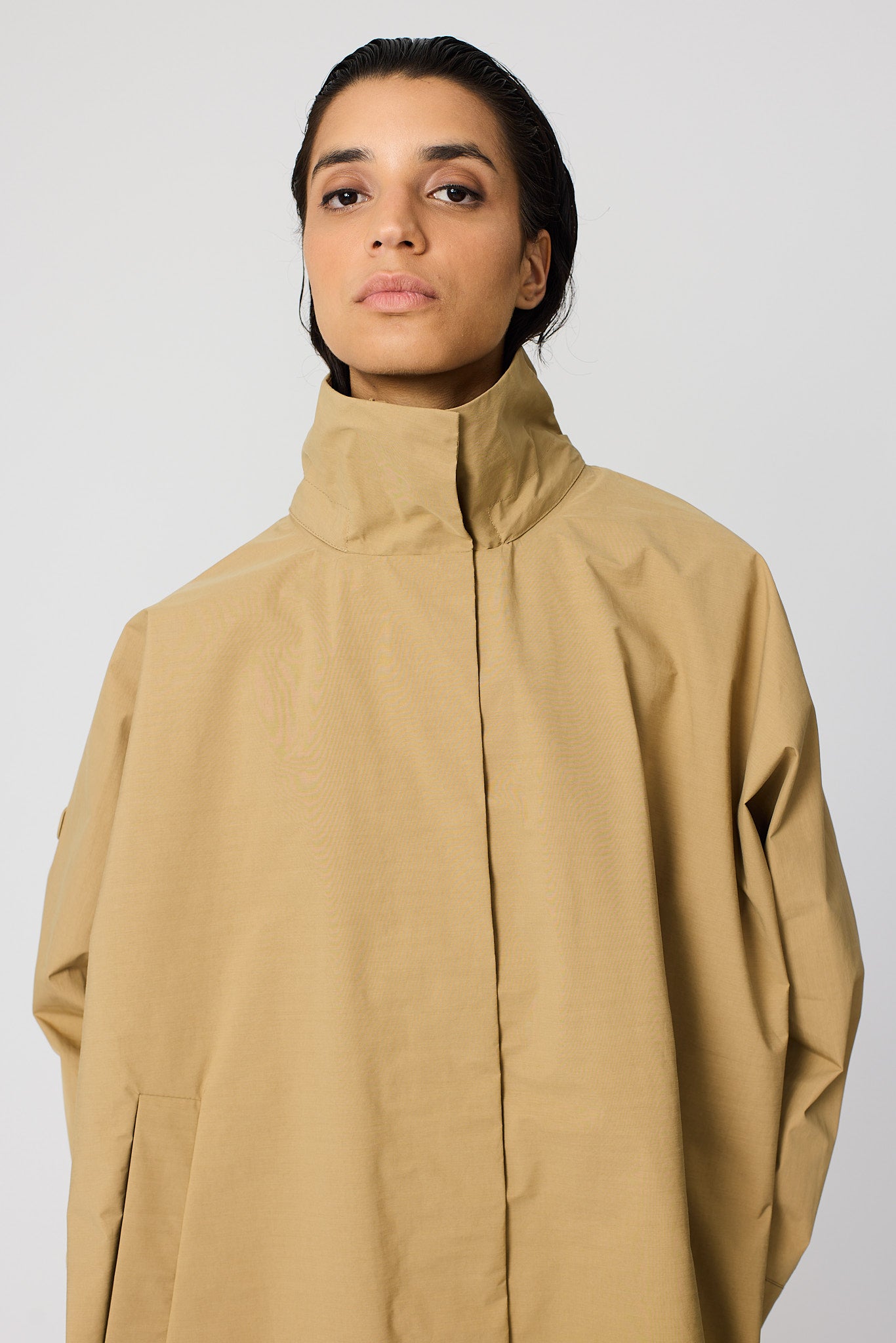 Person wearing a beige coat against a plain background