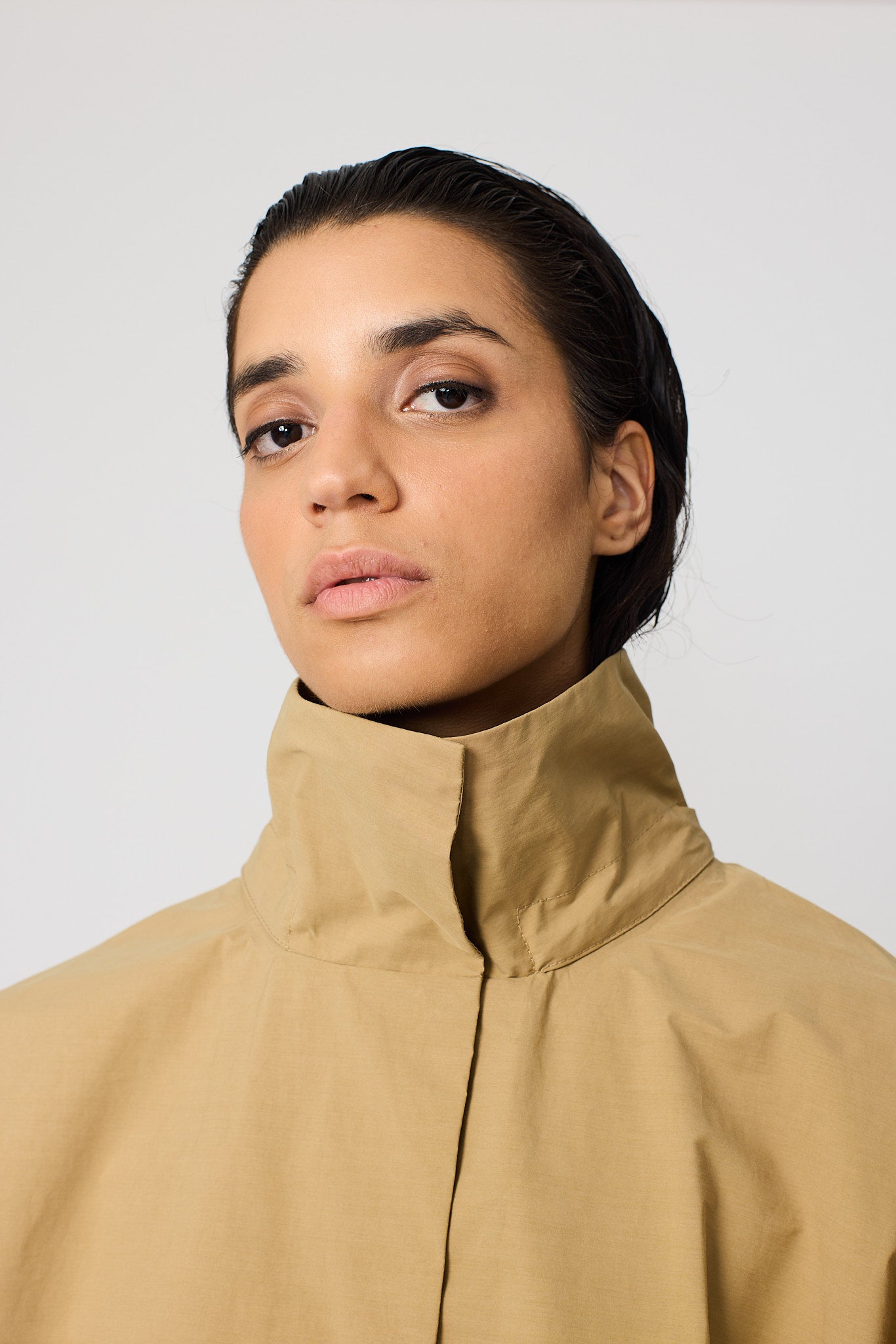 Woman wearing a beige raincoat against a plain background