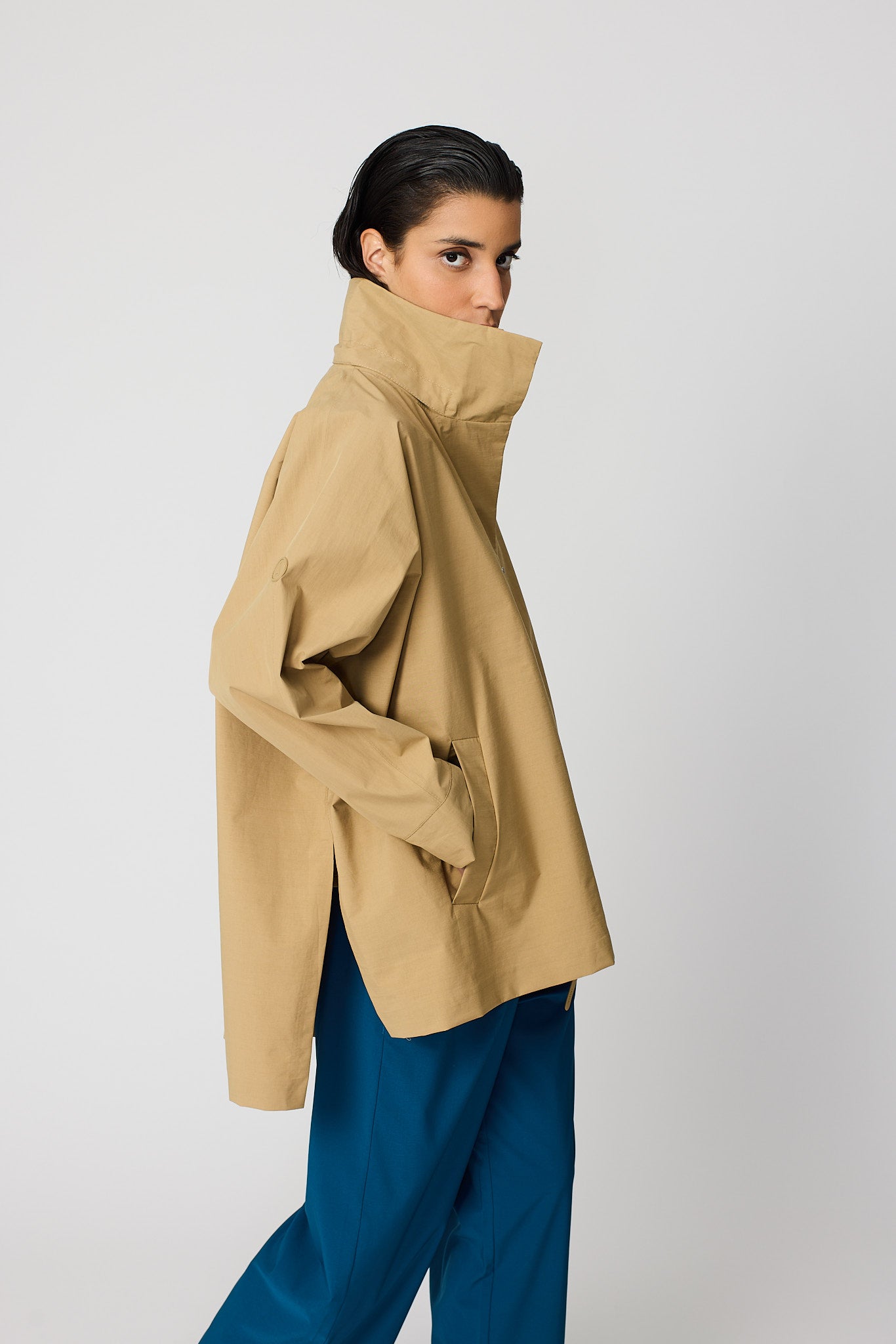 Person wearing a beige coat and blue pants on a white background