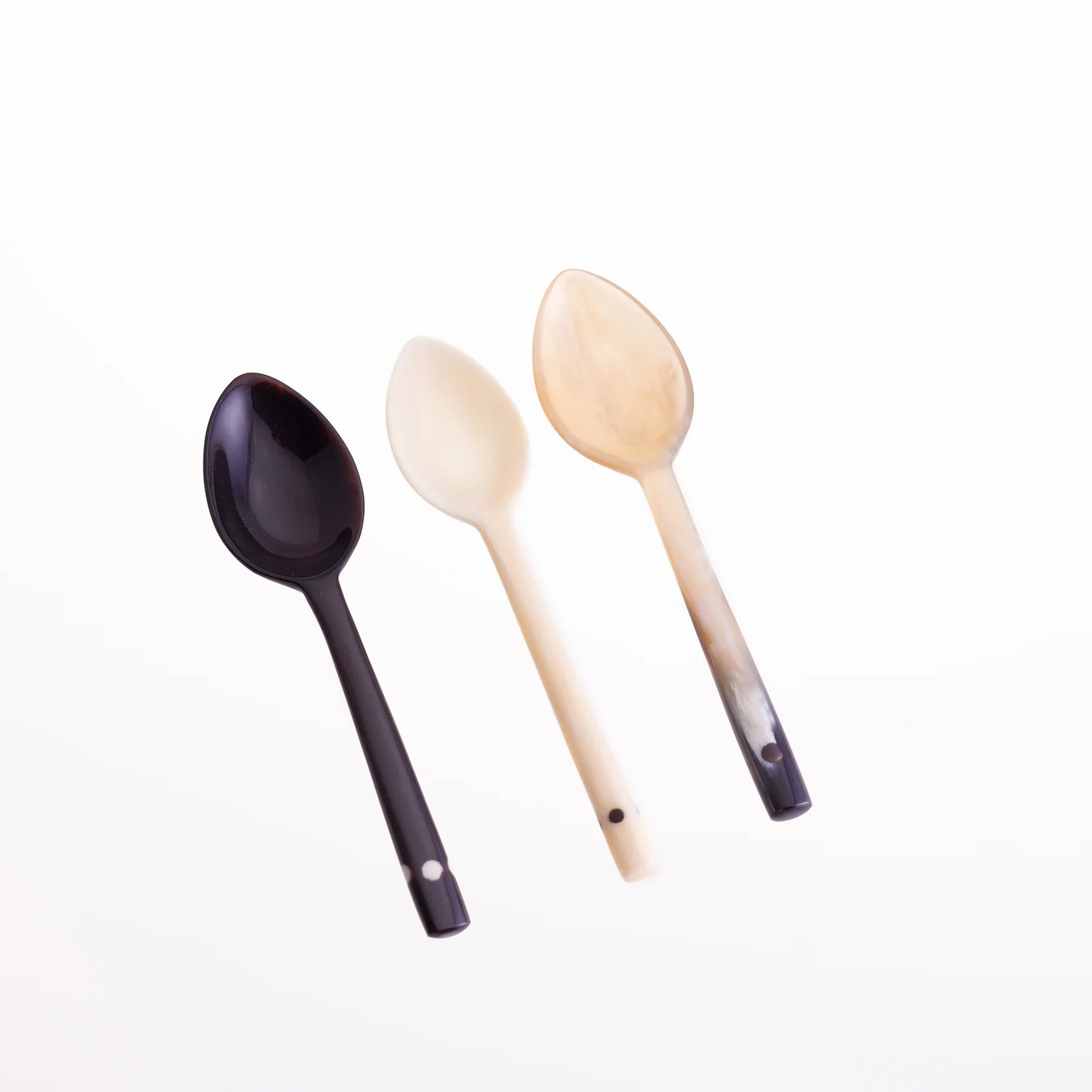 Three horn spoons in dark brown, light beige, and off-white.  Each spoon has a small dark dot near the handle end.