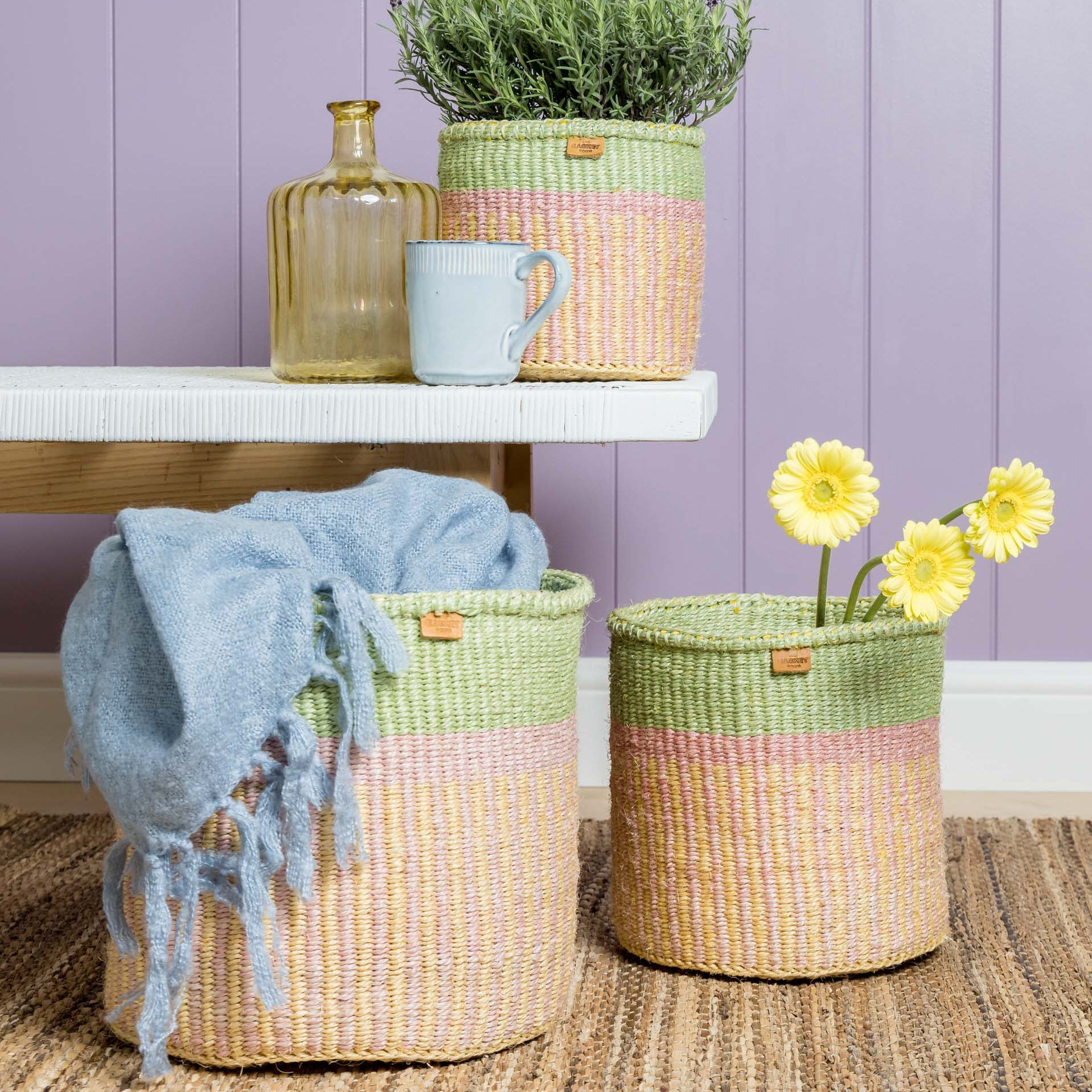 Three pastel-colored woven baskets; two large cylindrical baskets with a pale green and pink striped design, one containing