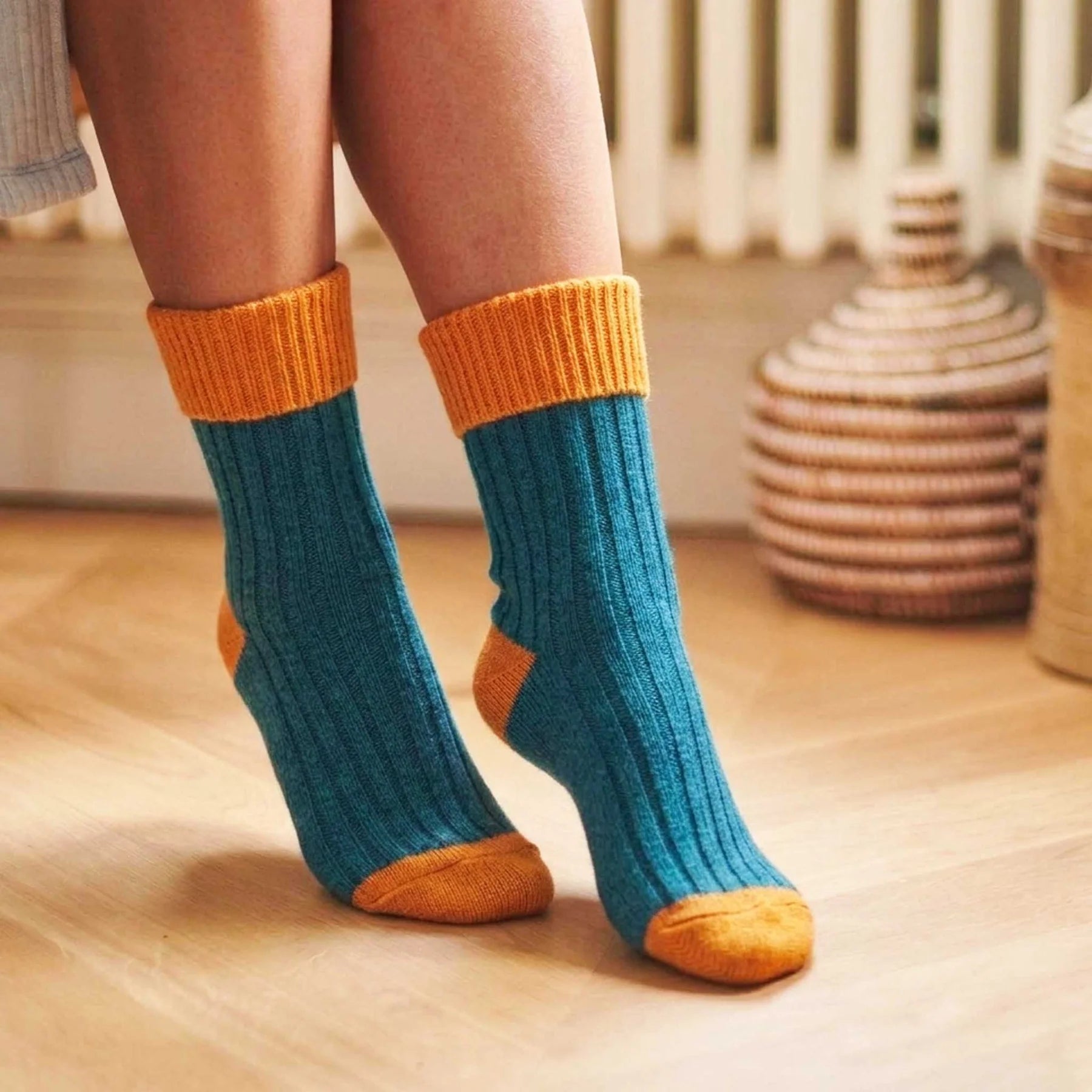 Teal socks with orange cuffs and toes worn by a person on a wooden floor.