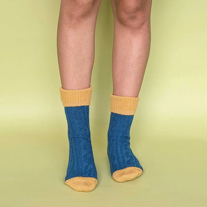 Blue socks with yellow cuffs and toes worn by a person on a green background