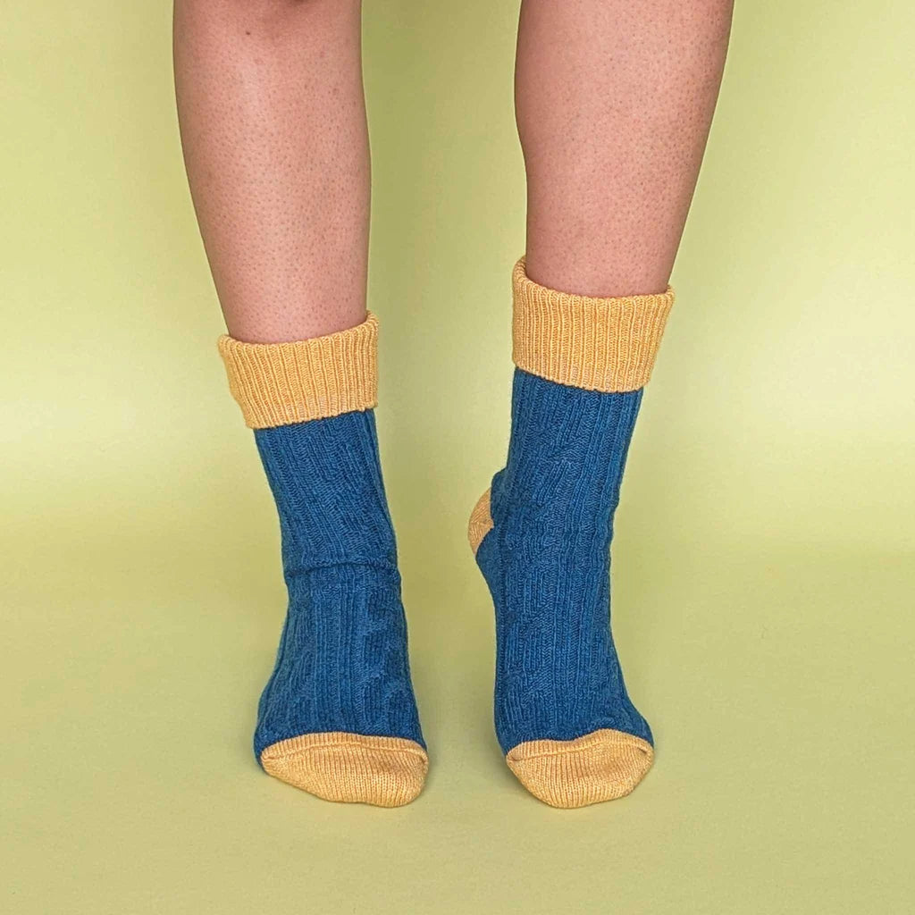 Blue socks with yellow cuffs and toes worn by a person on a green background