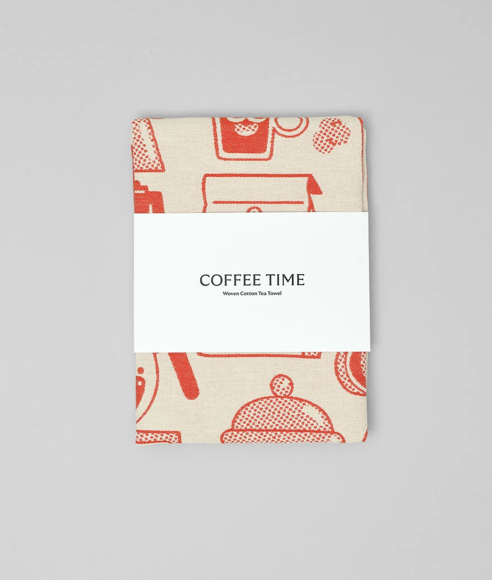 A folded woven cotton tea towel with a warm beige background and coral-red coffee-themed illustrations, wrapped in a white paper band labeled 'COFFEE TIME' against a neutral gray background.