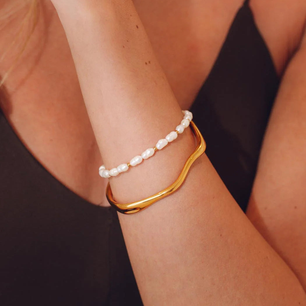 Gold bracelet and pearl bracelet on a person's wrist against a black background