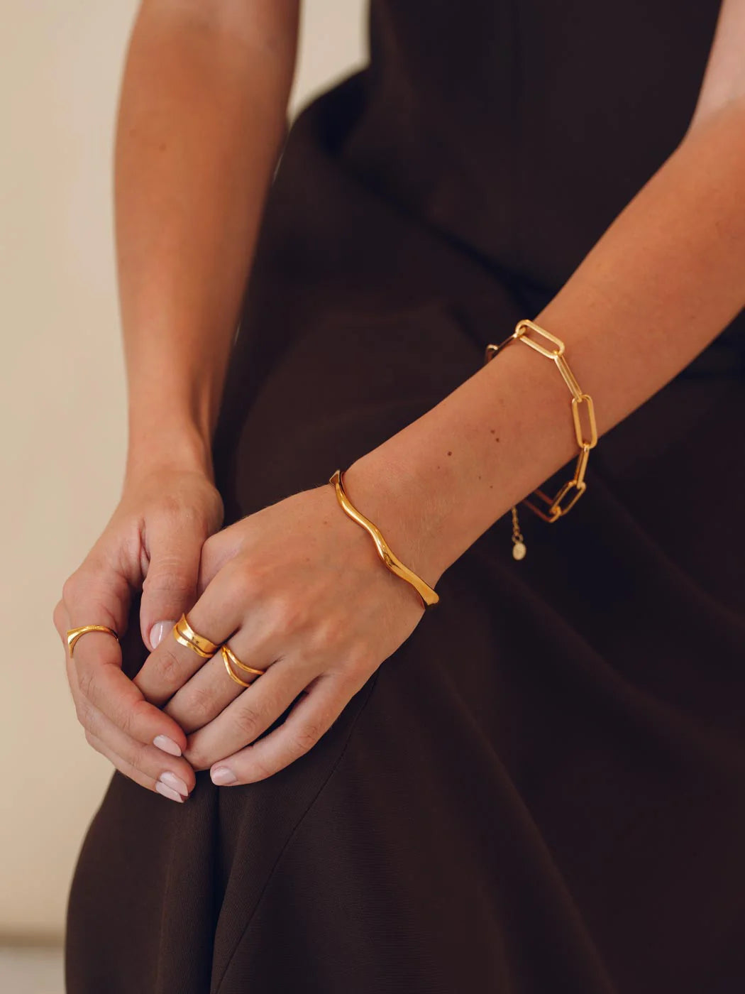 Close-up of a person wearing gold bracelets and rings on a plain background