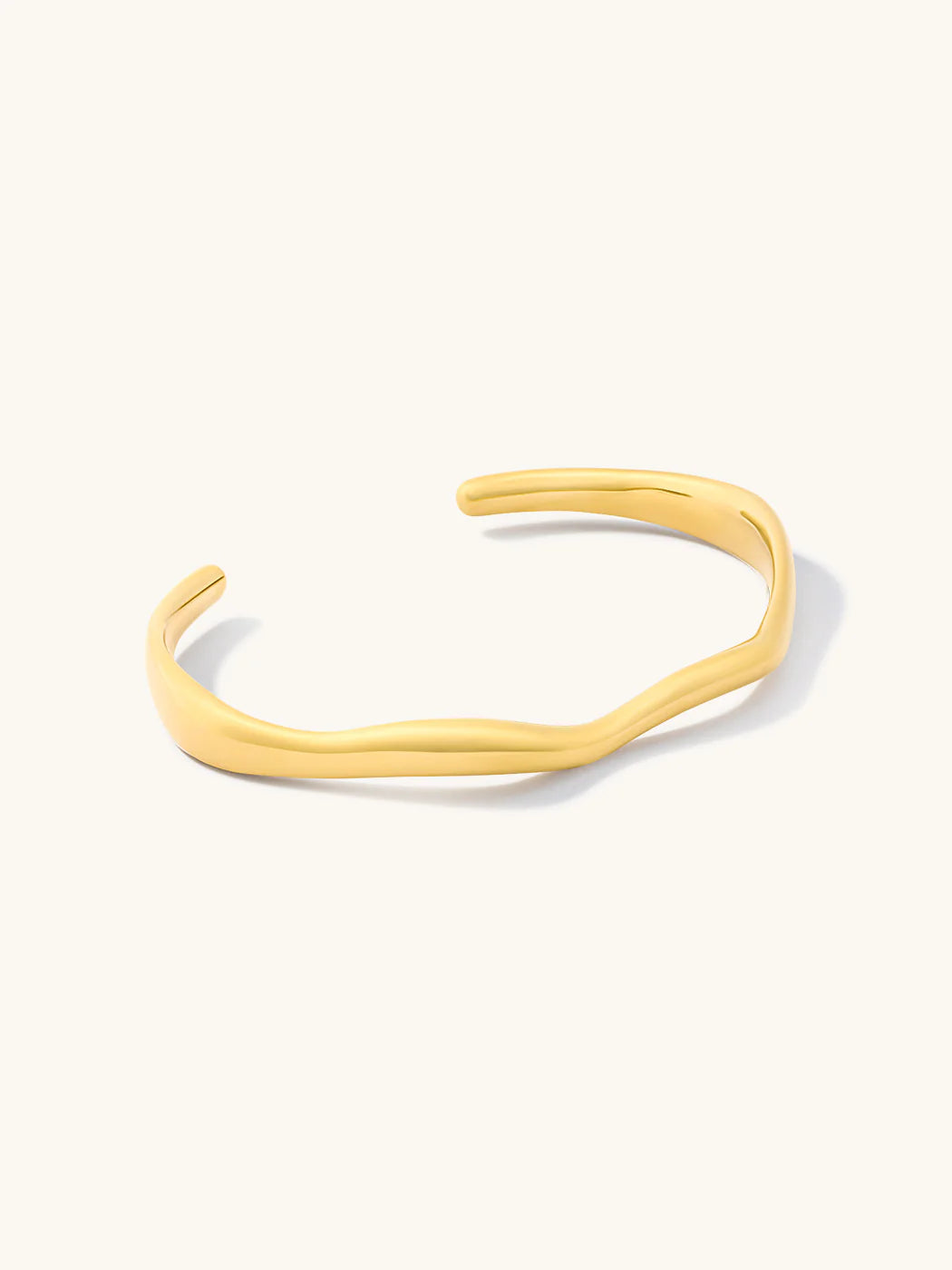 A polished gold-toned open cuff bangle bracelet with a wavy, organic silhouette, displayed on a clean off-white background.