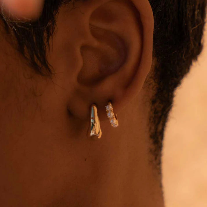Close-up of an ear with gold hoop earrings on a blurred background