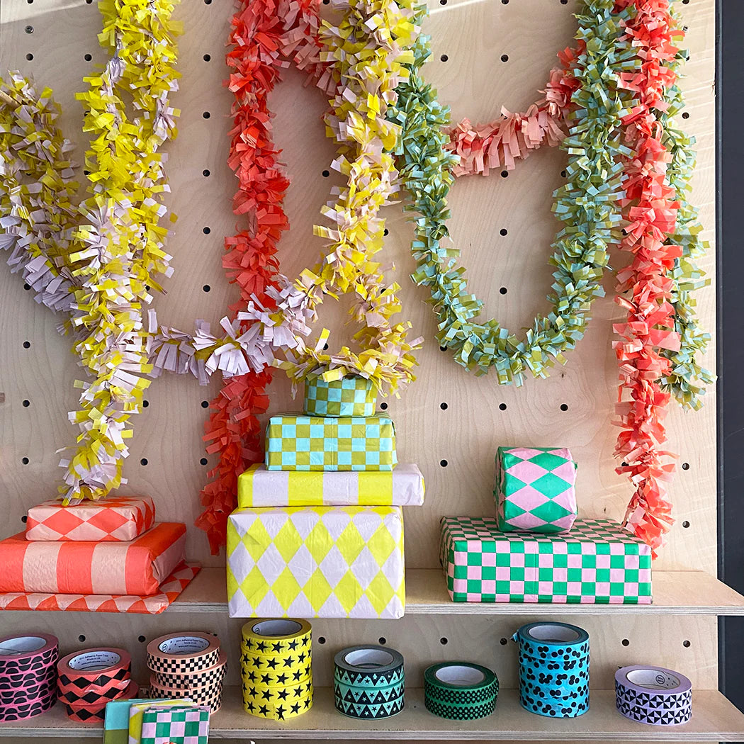 Colorful paper garlands and stacks of gift wrap in various geometric patterns, plus rolls of decorative washi tape.