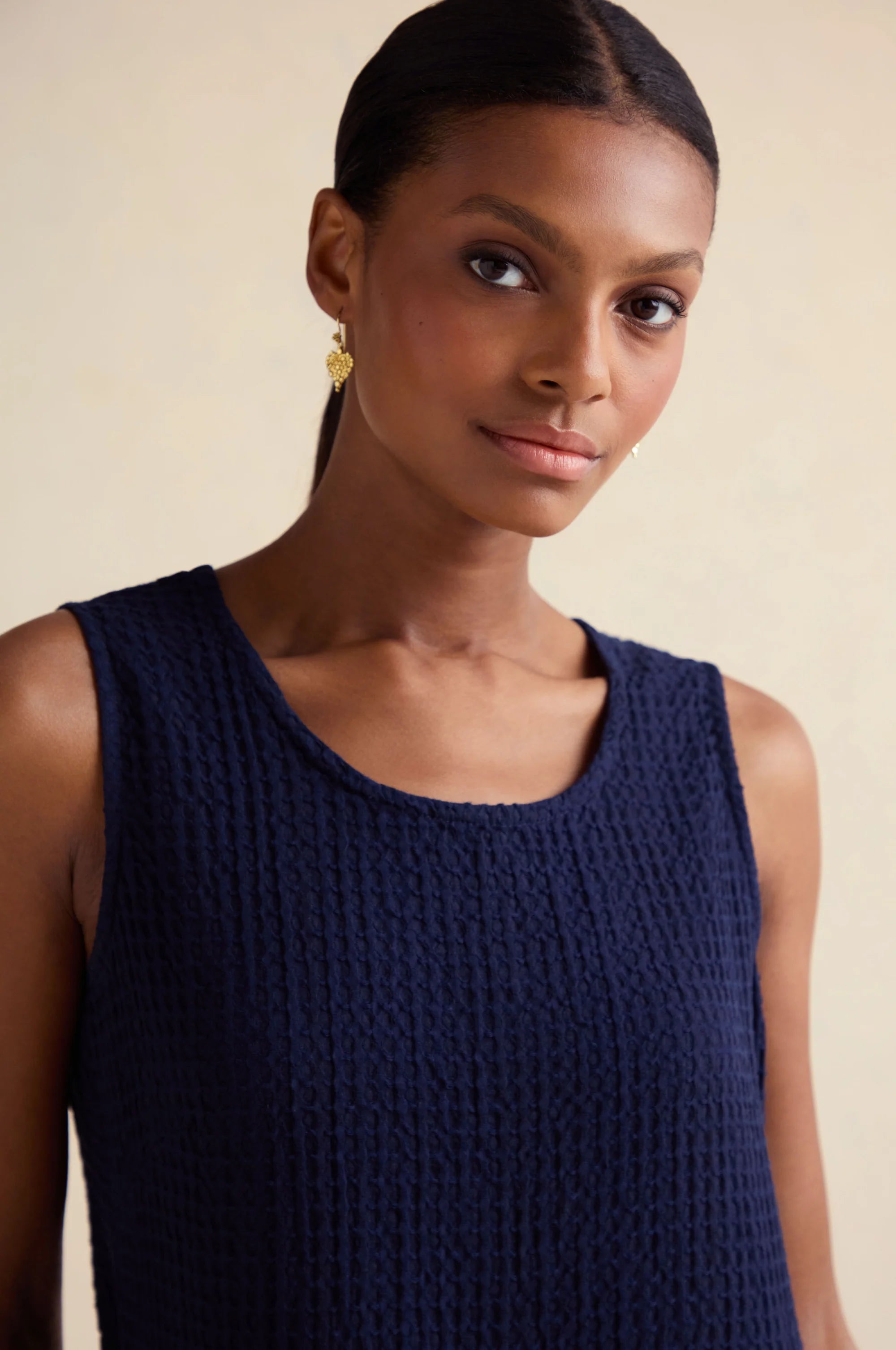 Woman wearing a navy blue sleeveless top against a beige background