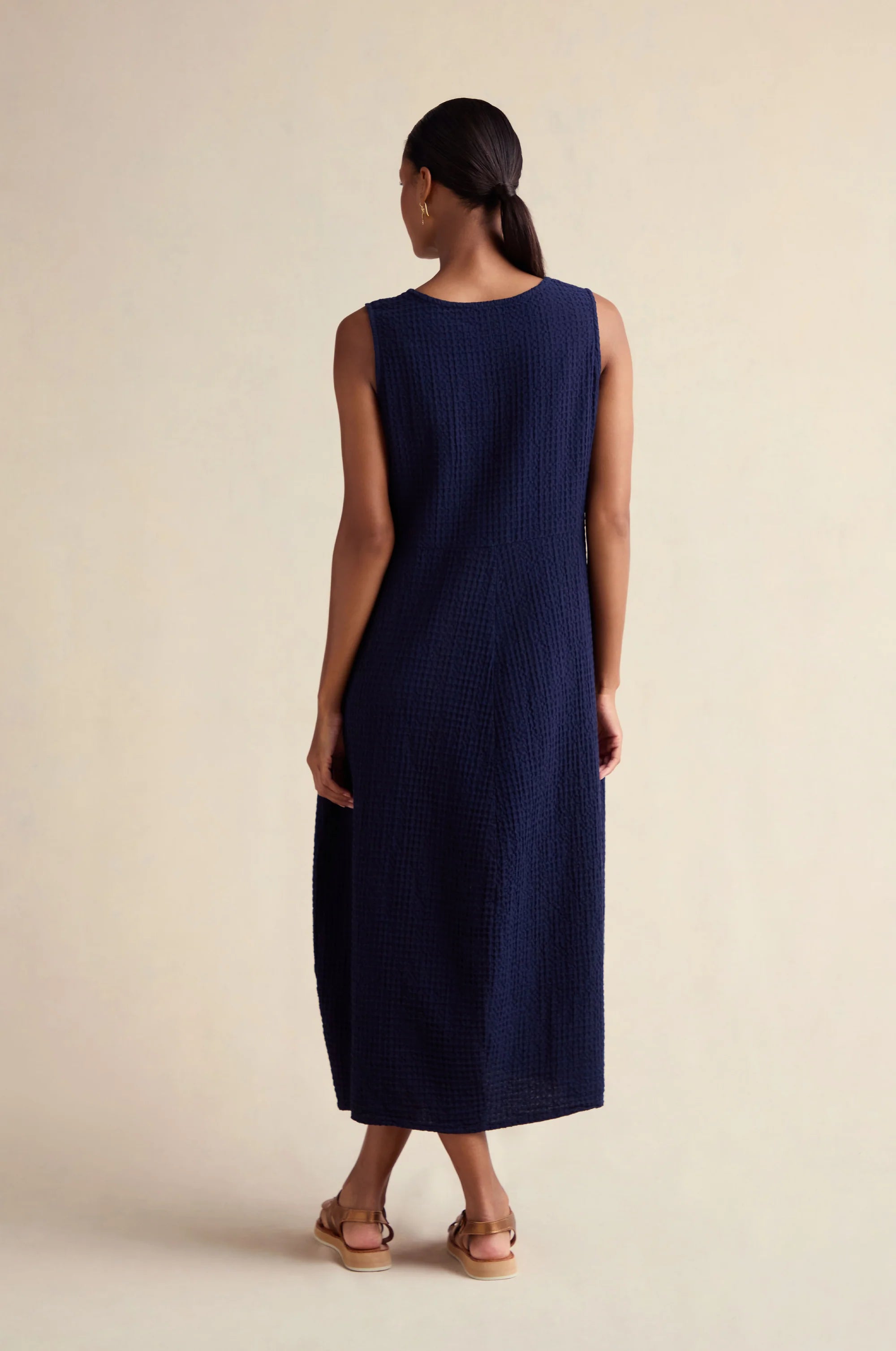 Woman wearing a navy sleeveless dress against a beige background