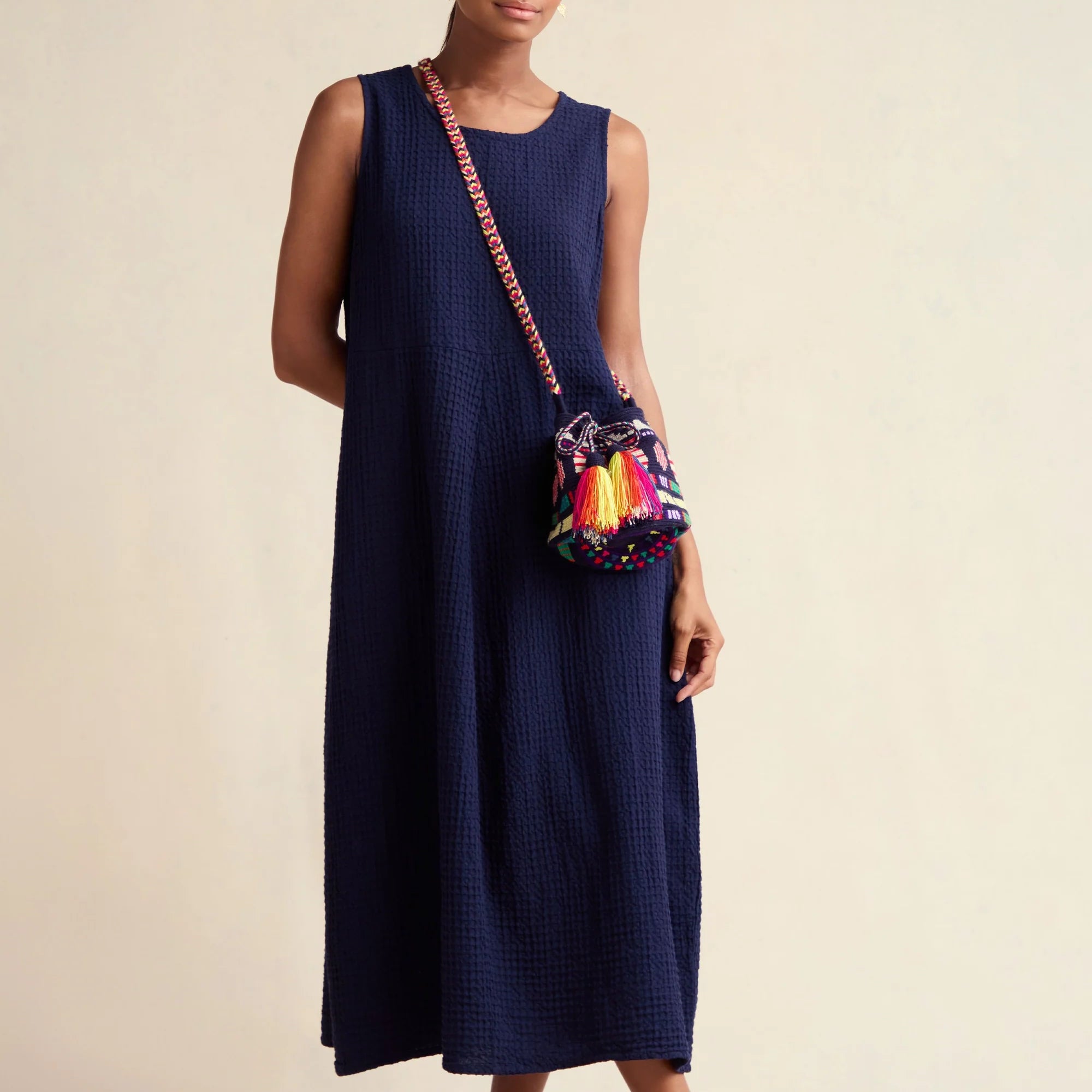 Woman wearing a navy sleeveless dress with a colorful bag on a beige background