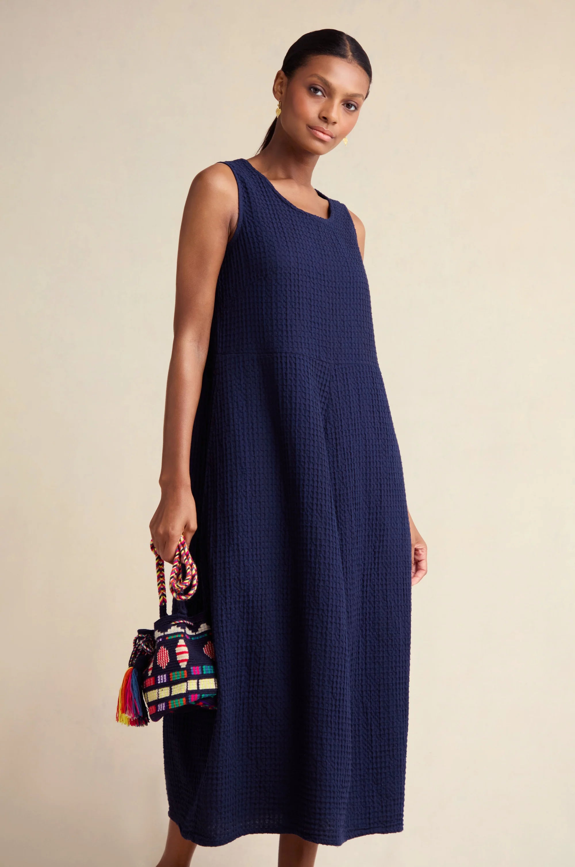 Woman wearing a navy sleeveless dress holding a colorful handbag against a beige background