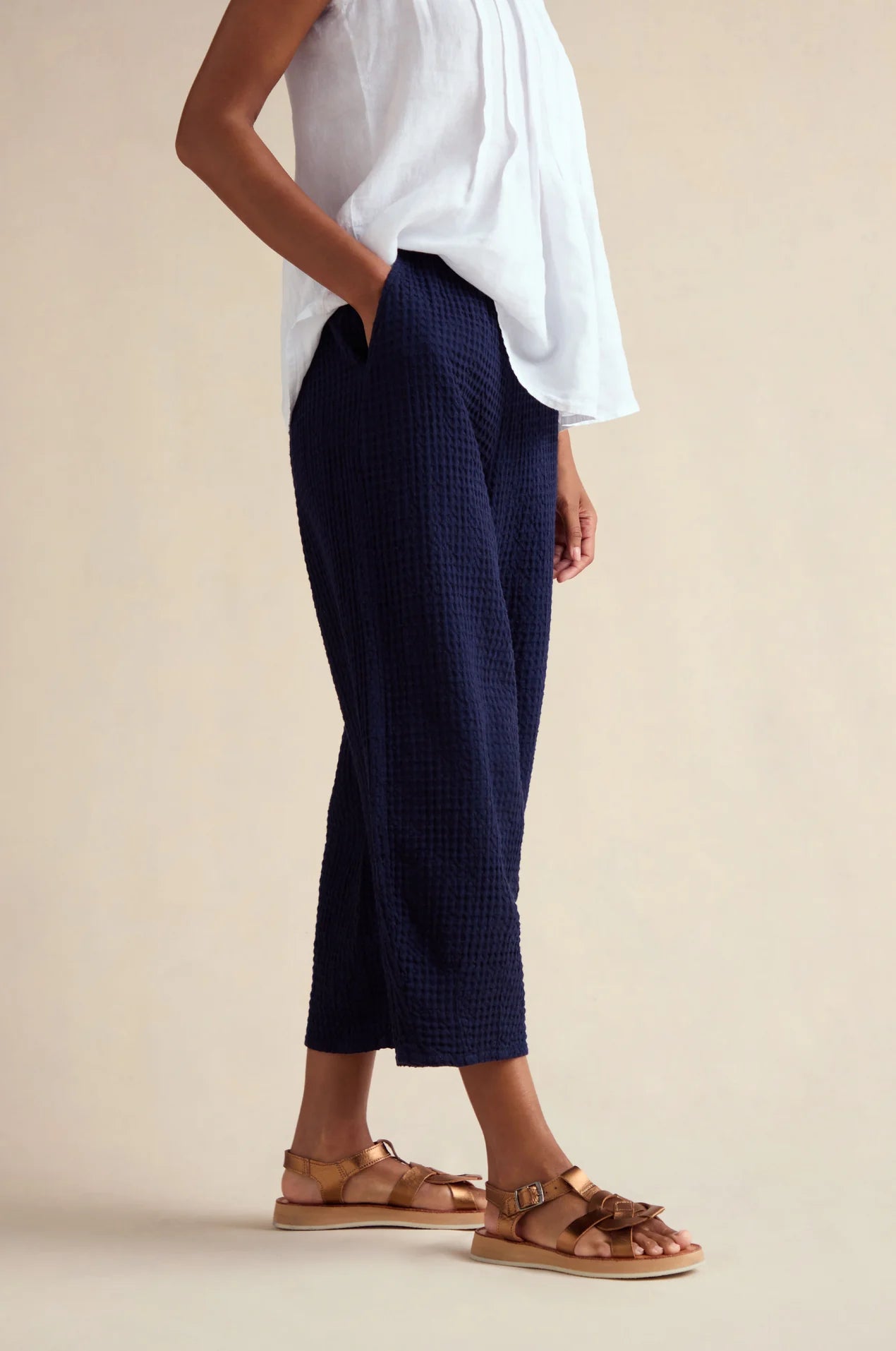 Person wearing navy checkered pants and white top on a beige background