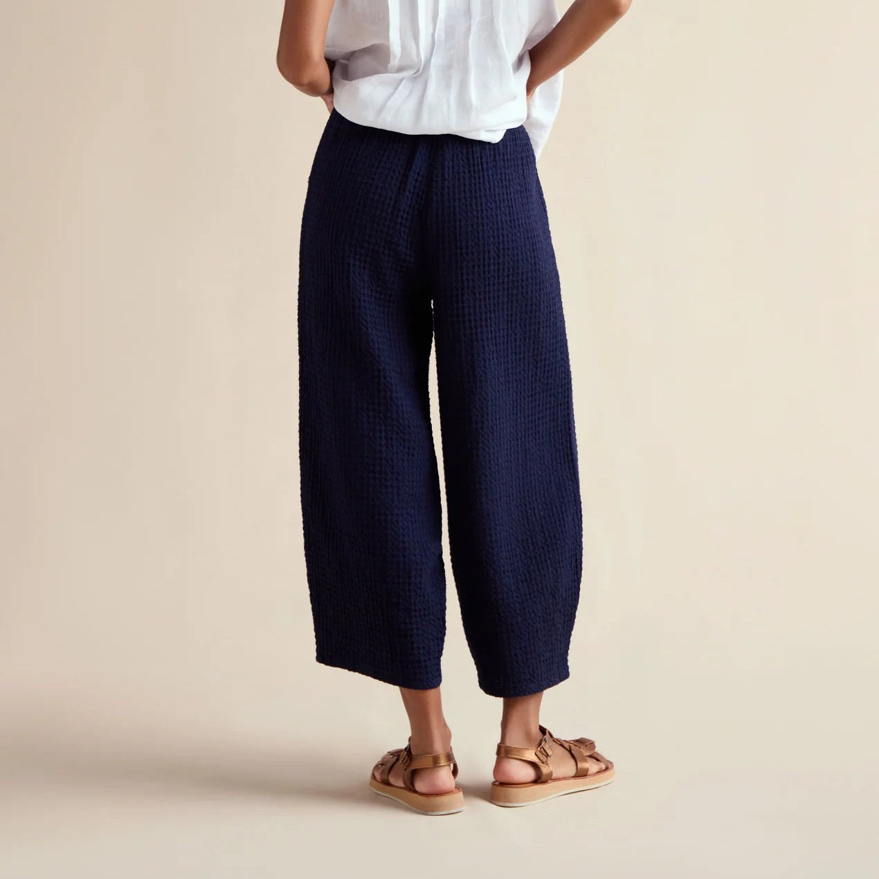 Woman wearing a white sleeveless top and navy pants on a beige background