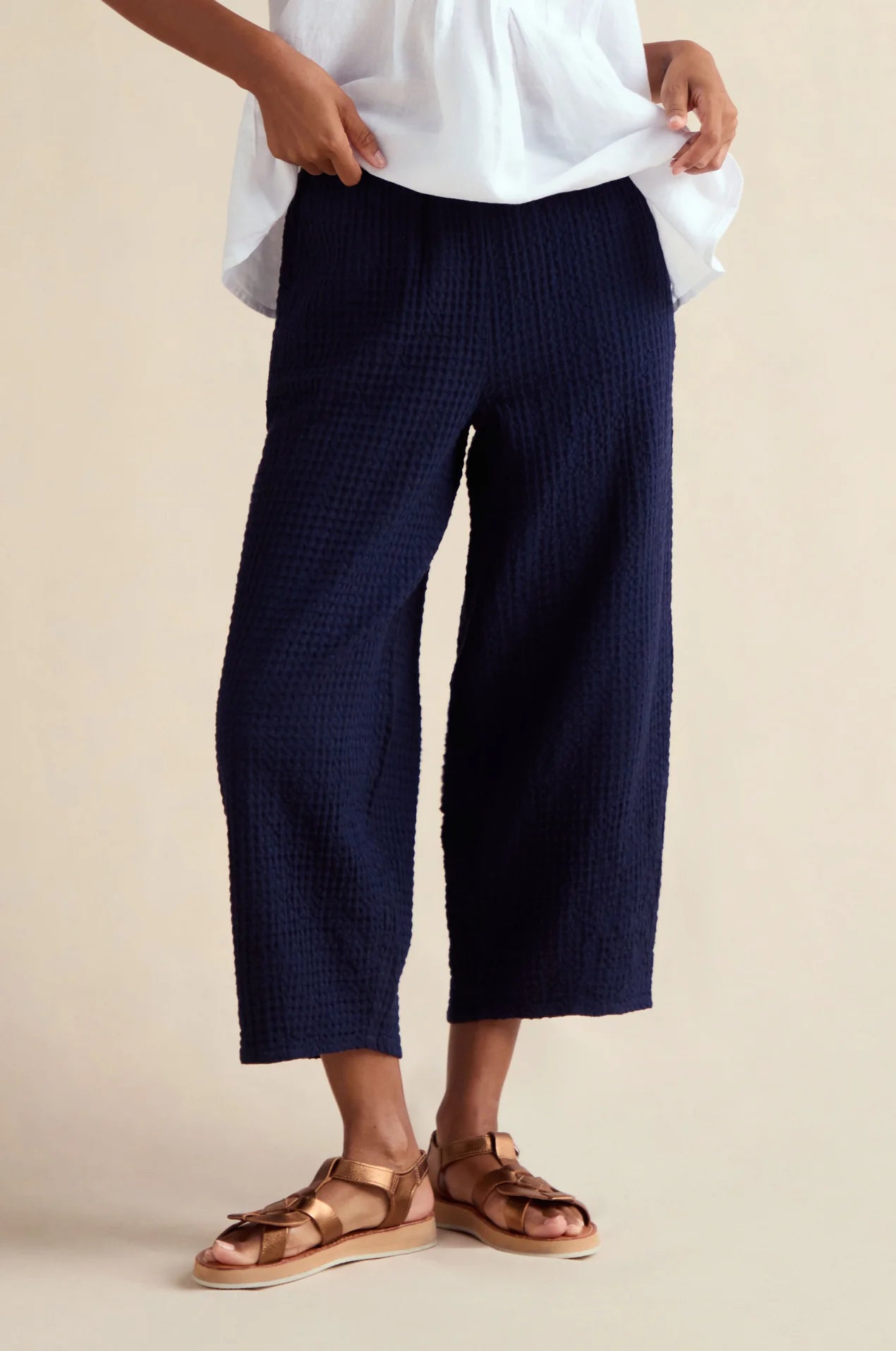 Person wearing navy checkered pants and white shirt on a beige background