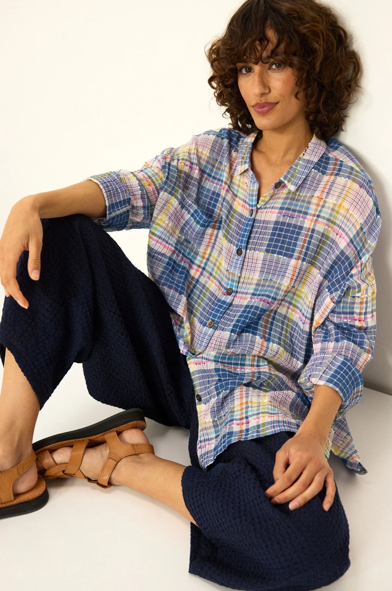 Woman wearing a plaid shirt and dark pants sitting on a white floor.