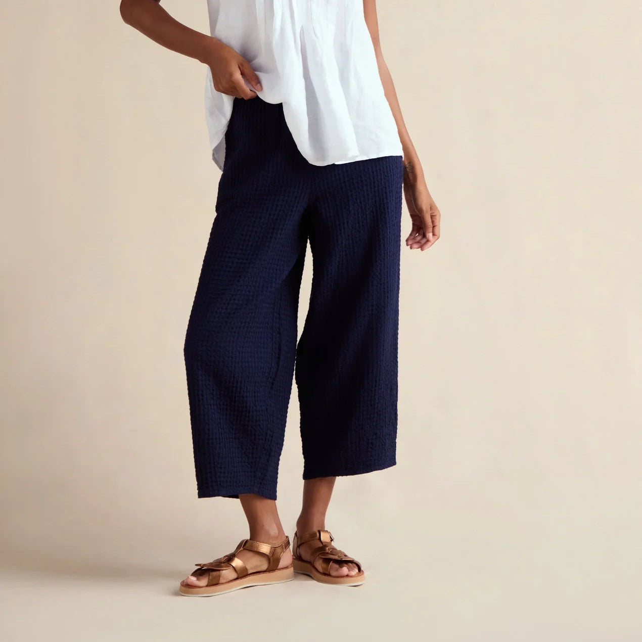 Woman wearing a white sleeveless top and navy pants on a beige background