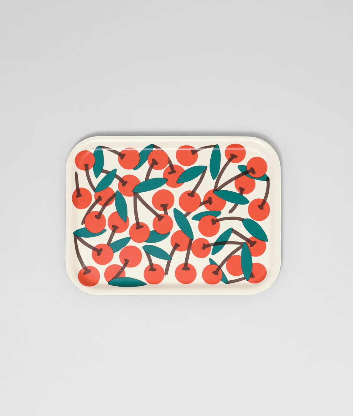 A rectangular tray with rounded corners featuring a repeating pattern of red cherries with dark brown stems and teal-green leaves on a light cream background, set against a solid light gray studio backdrop.