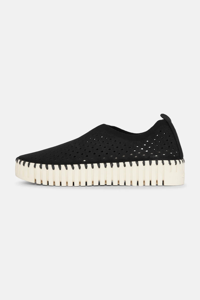 Black slip-on sneaker with perforated upper, off-white textured sole, and black stitching detail.