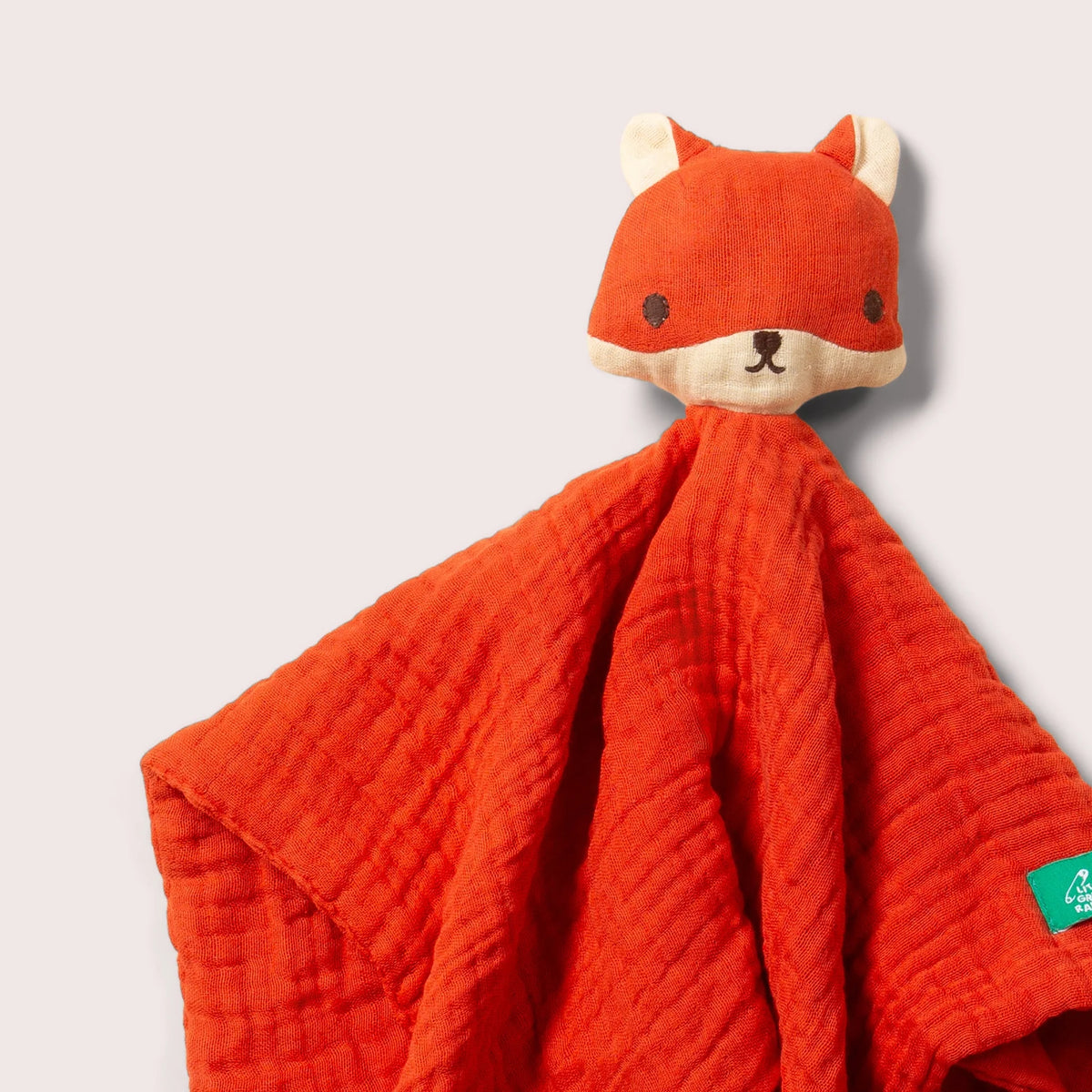 A baby security blanket featuring a textured orange-red muslin fabric body and a plush fox head attachment in matching orange-red with cream accents, shown against a light gray background.