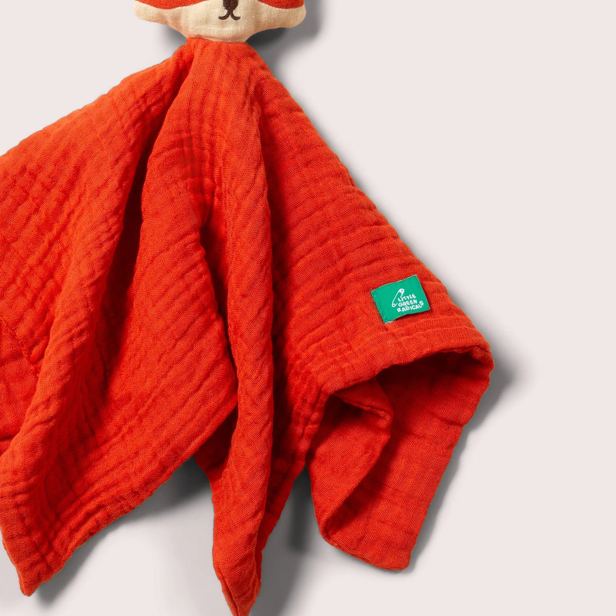 A close-up of a textured red muslin security blanket with a plush fox head handle, featuring a small green 'Puppy Paws' brand tag.