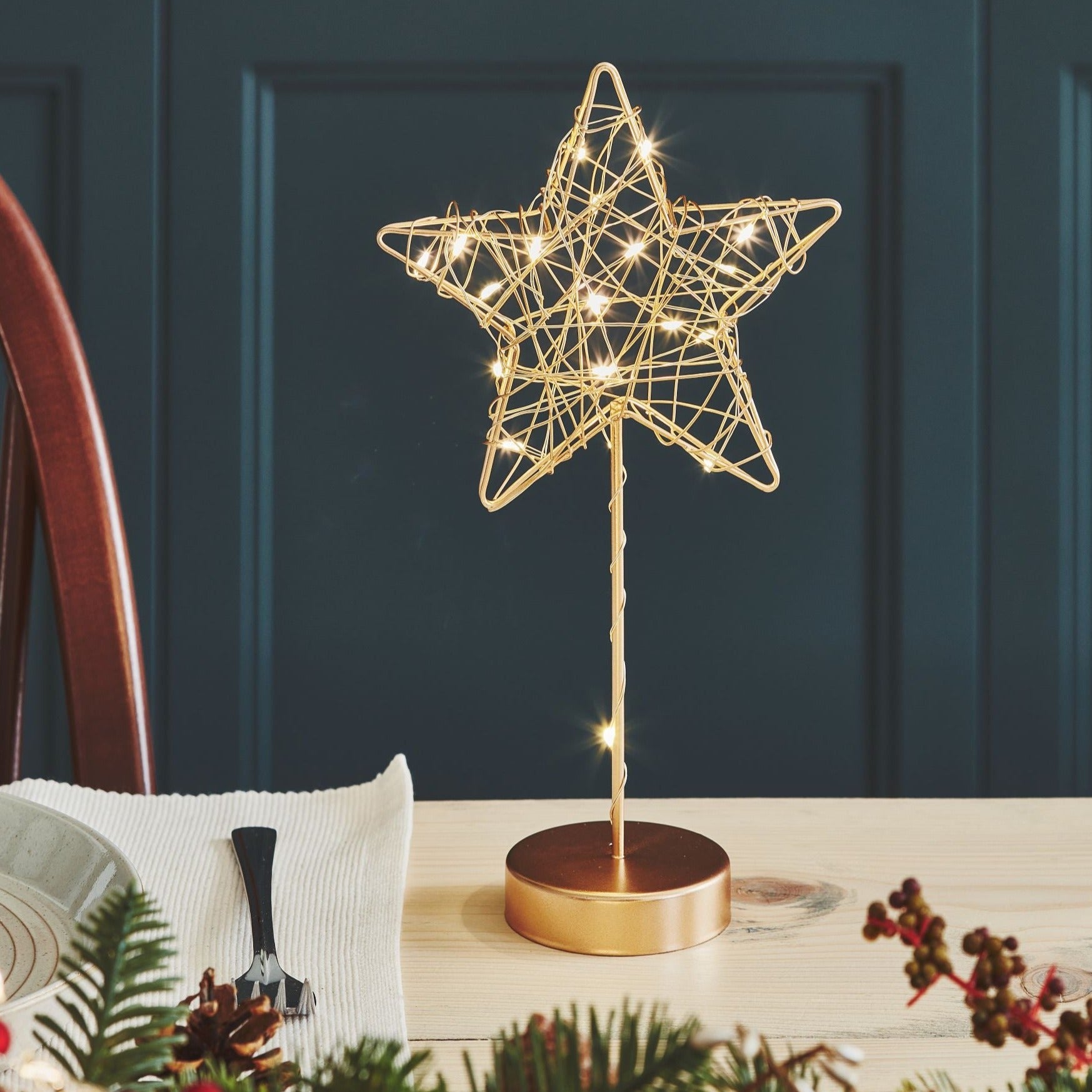 Gold wire star table decoration with integrated LED lights.  The star sits on a gold base and has a slender gold stem.