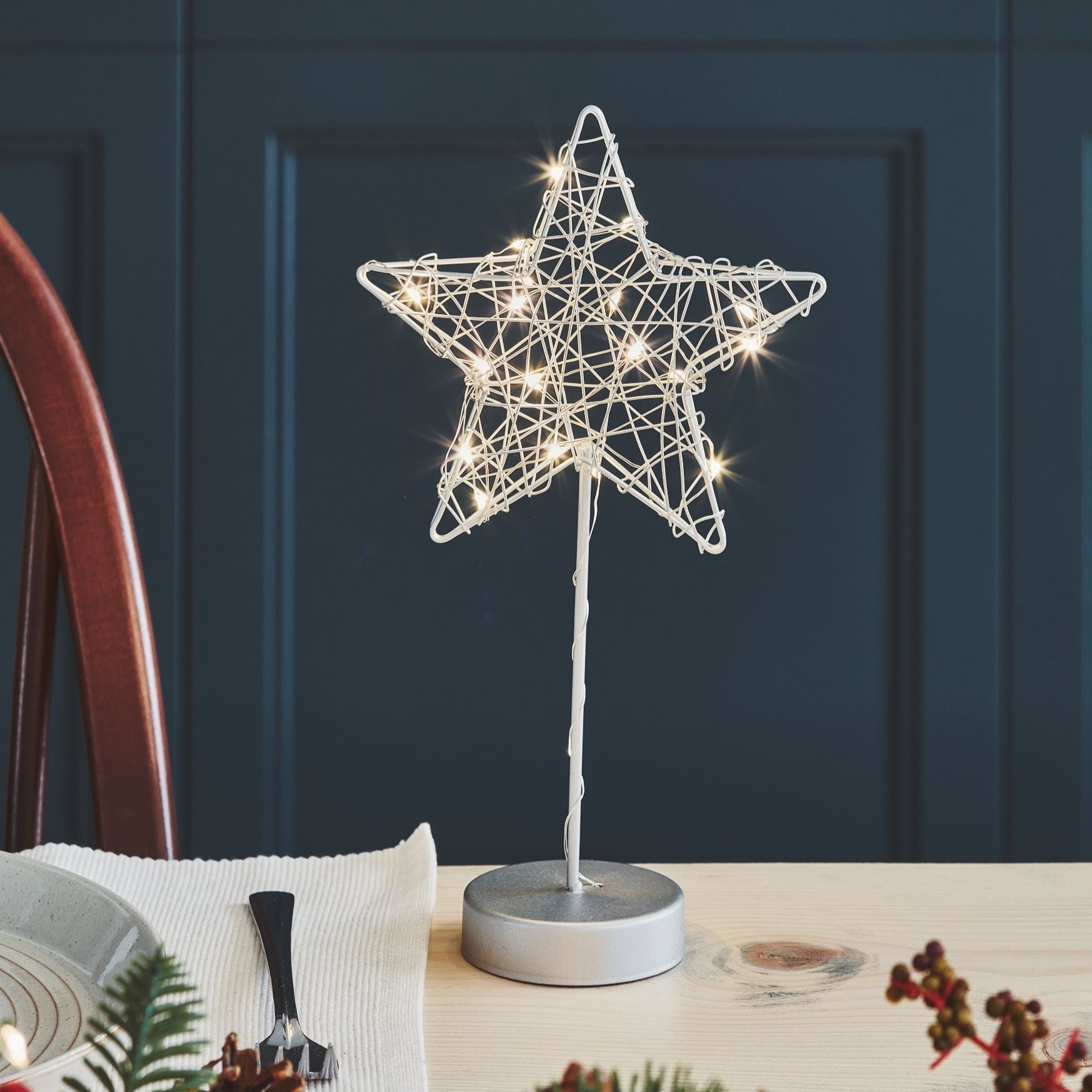 White wire star table lamp with warm white LED lights.  The star sits atop a silver base.