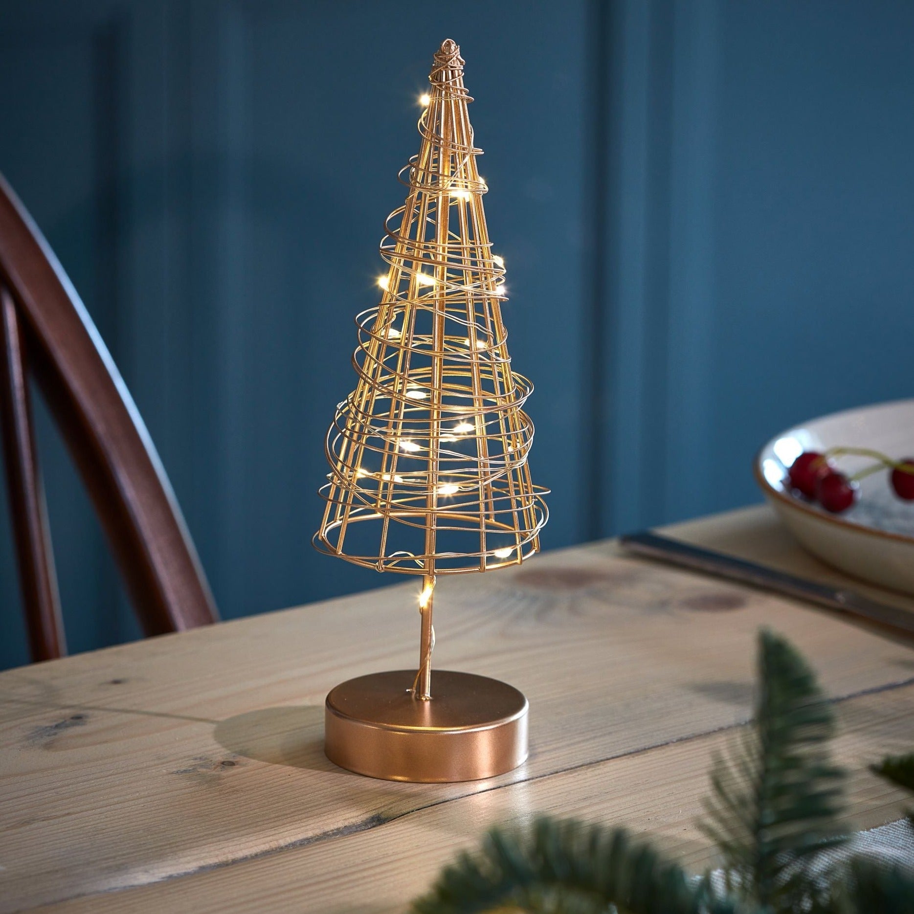 Gold metal wire Christmas tree with integrated warm white LED lights, standing on a copper-colored base.