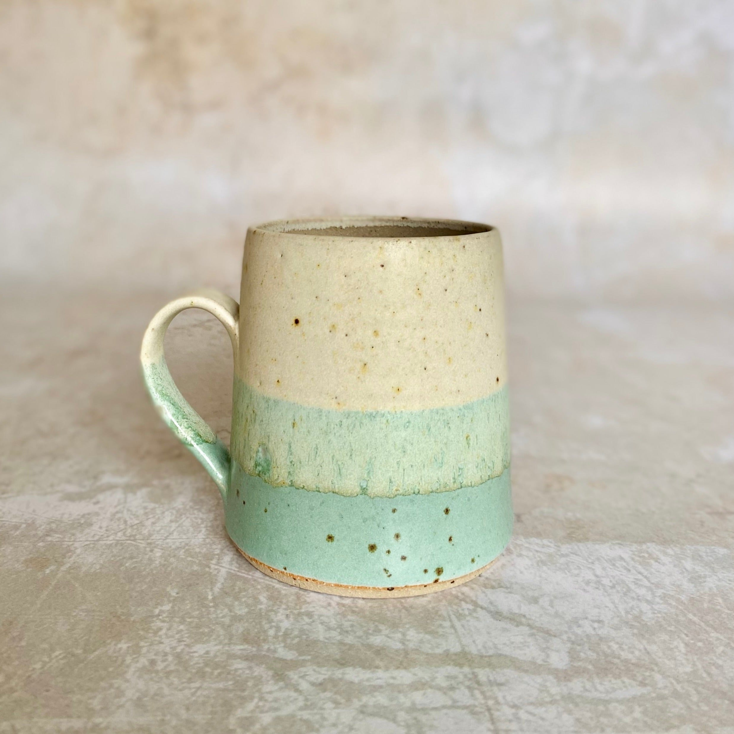 Hand-thrown stoneware mug with speckled off-white top and a light seafoam green bottom.