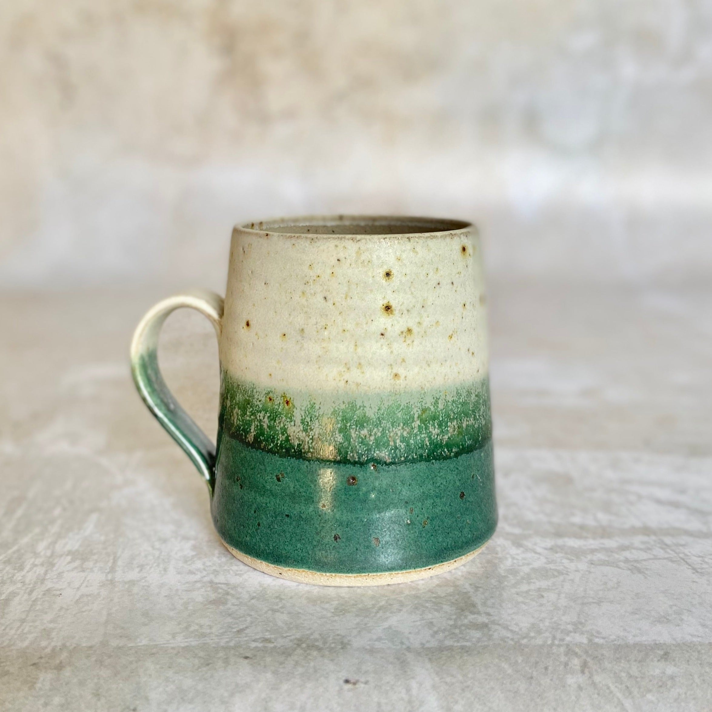Hand-thrown stoneware mug with a speckled off-white top and a teal bottom, separated by a subtle gradient.