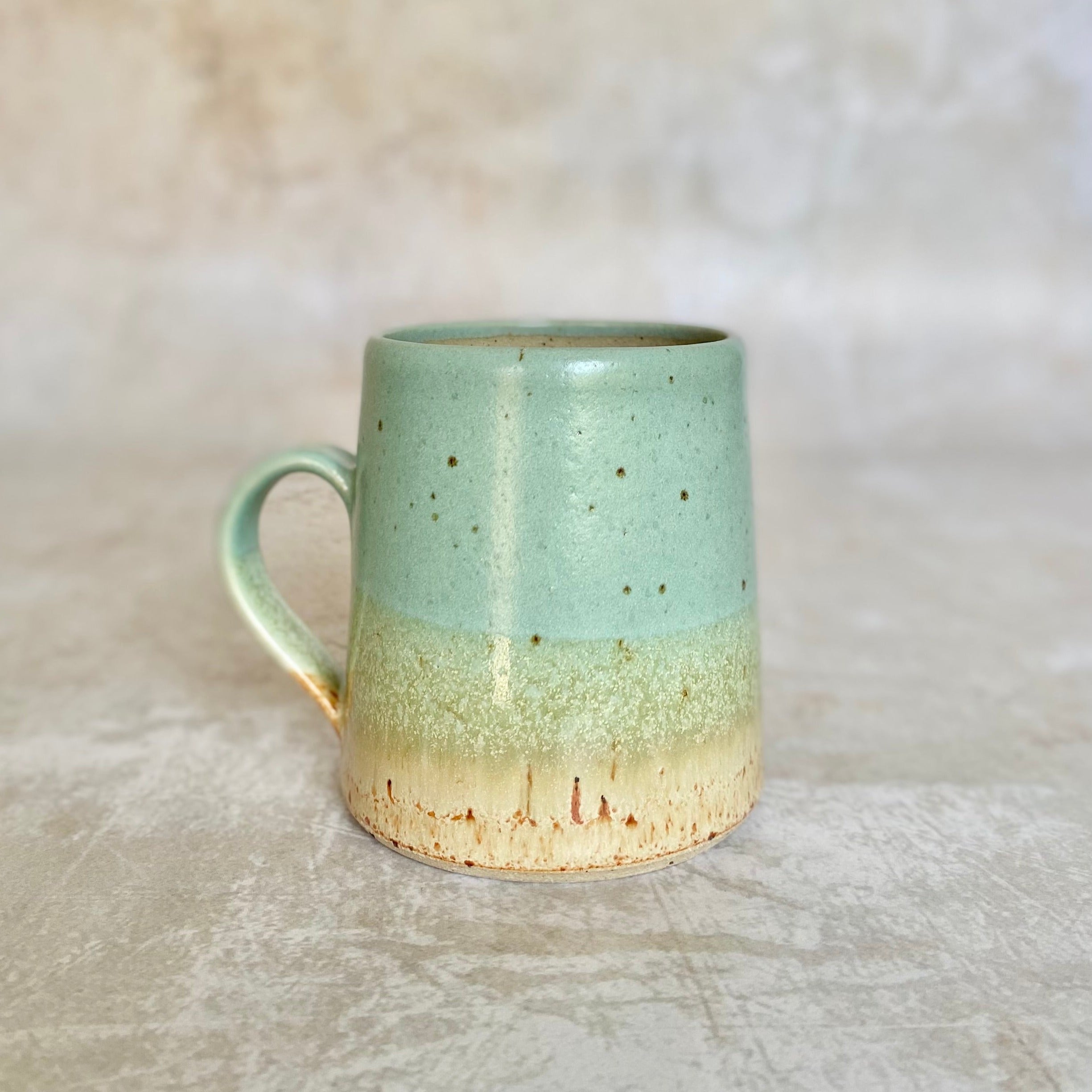 A speckled light-green and beige ceramic mug with a rounded handle.