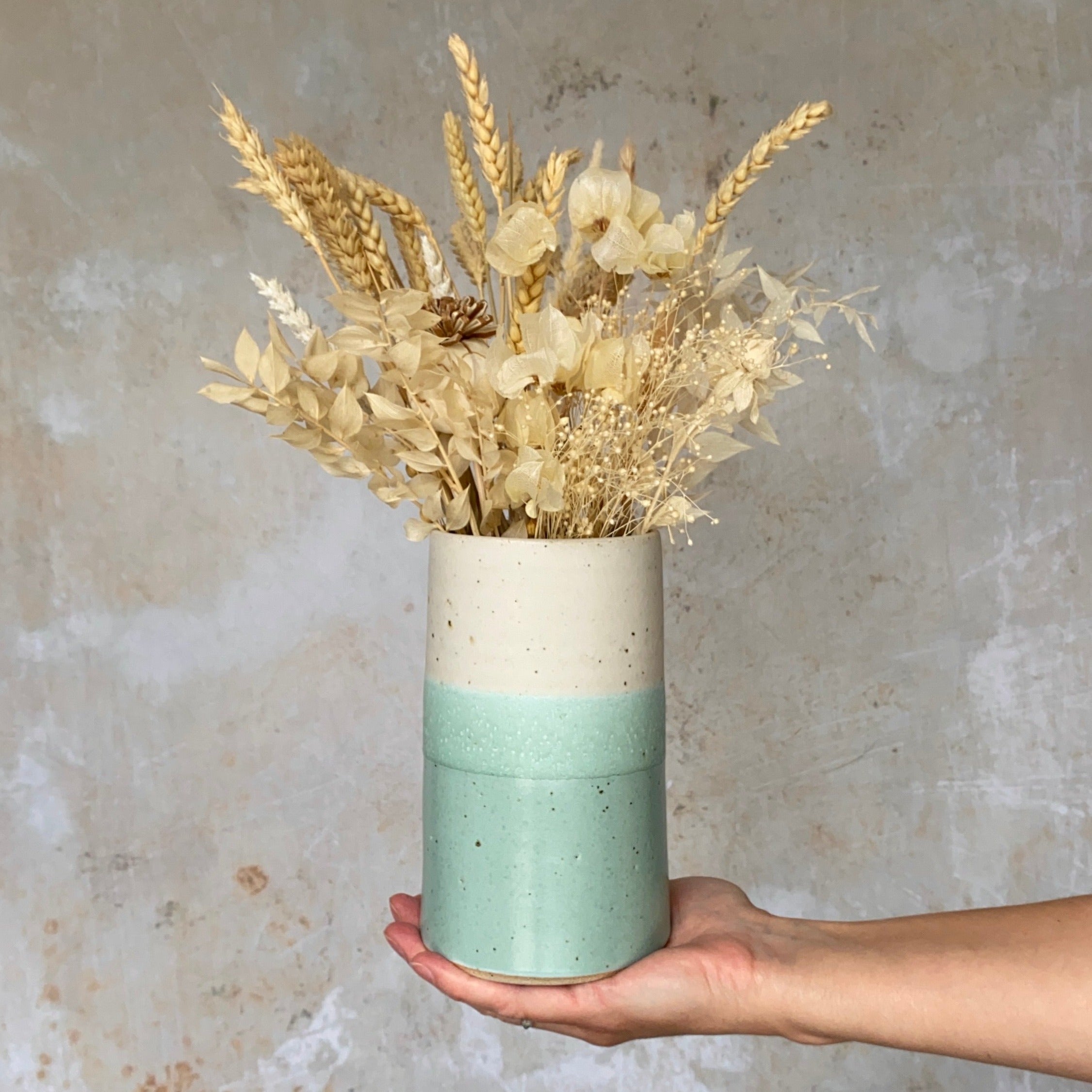 Speckled cream and light teal ceramic vase holding a bouquet of dried wheat, flowers, and grasses.